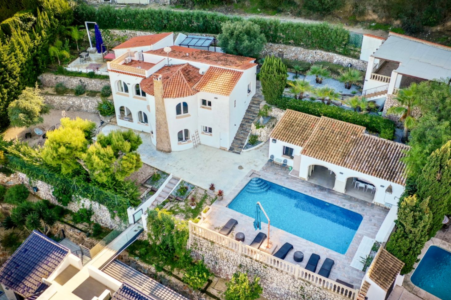 Luchtfoto van de mediterrane villa met zwembad, stenen zonneterrassen, buitenkeuken en aangelegde terrastuinen op een ruim, privé perceel.