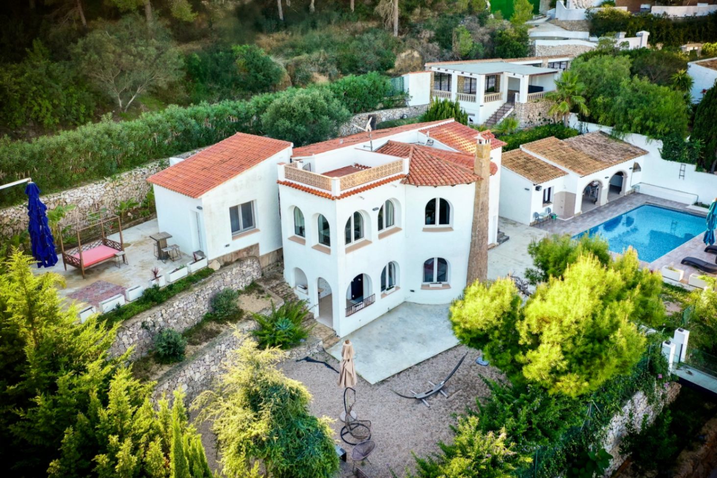 Luchtfoto van de villa met witte gevels en terracotta daken, inclusief het zwembad, stenen terrasmuren en boogvensters in een bosrijke omgeving.
