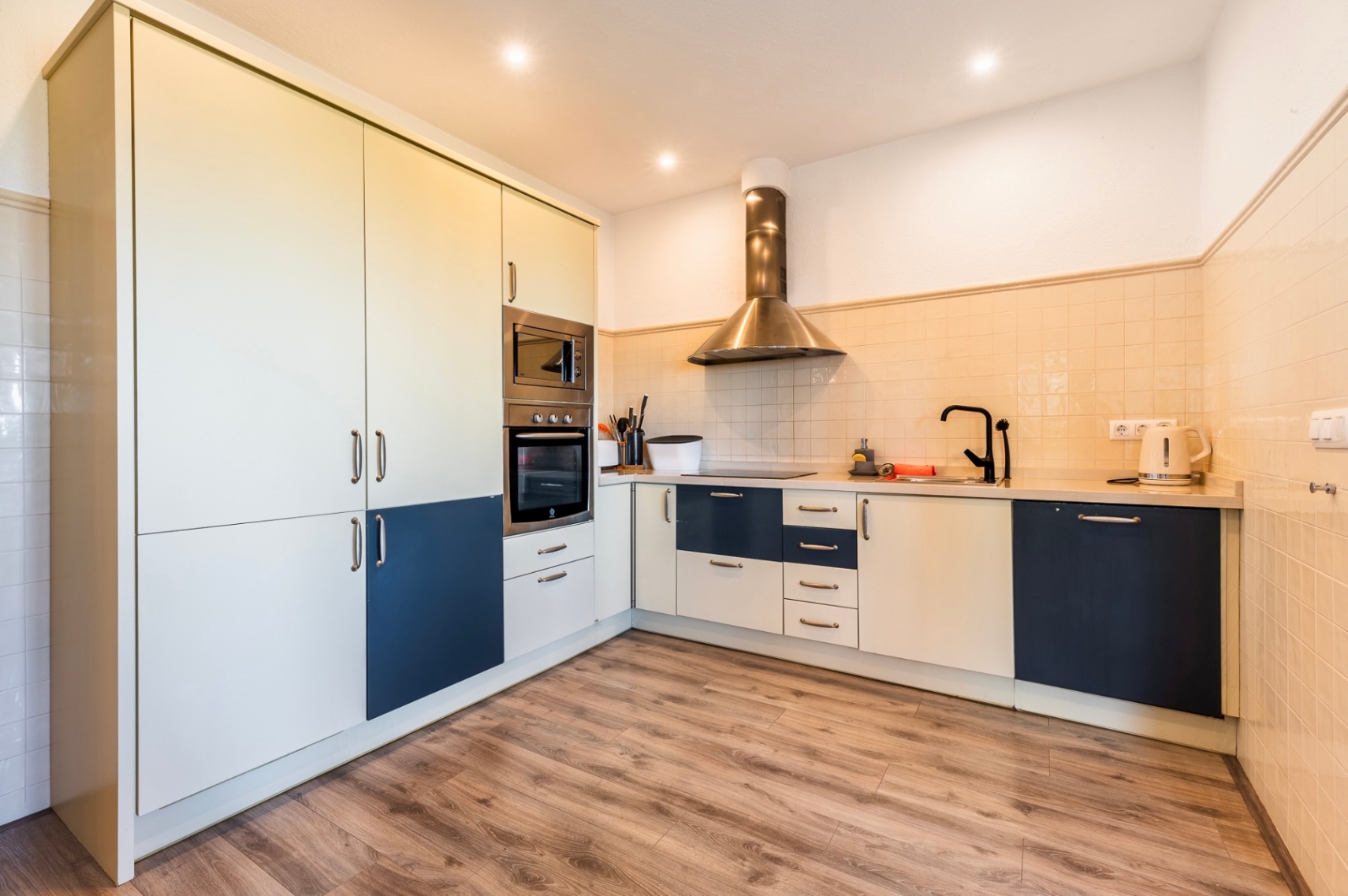 Moderne gerenoveerde keuken met tweekleurige kasten in blauw en crème, rvs-apparatuur en een vloer met houtlook.