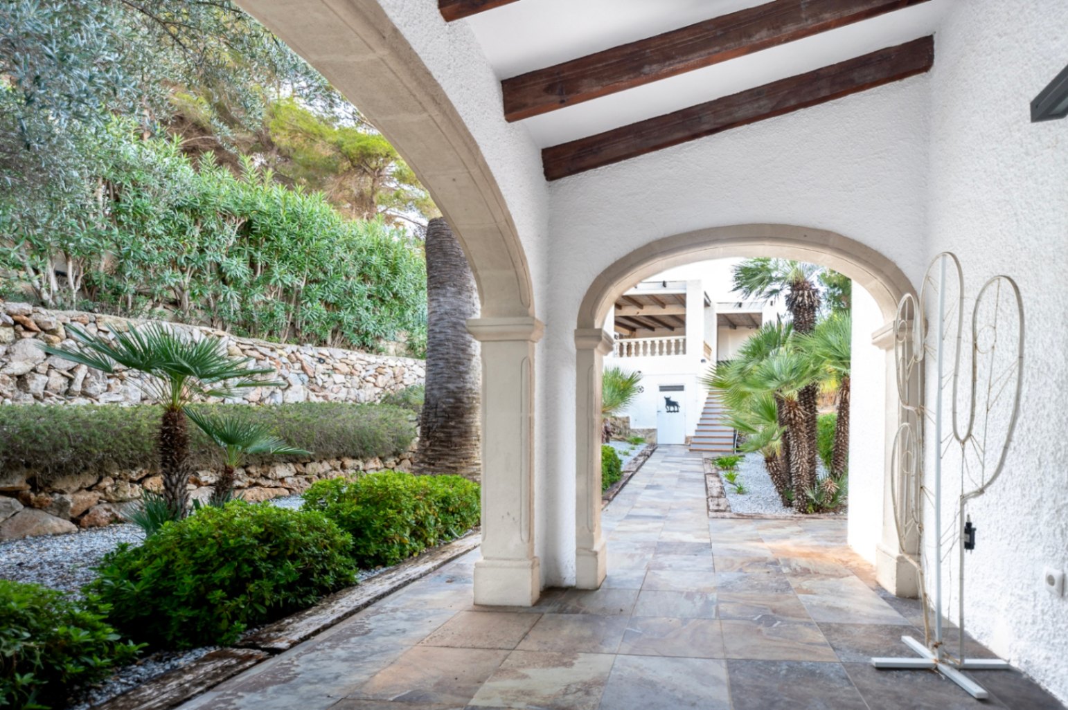 Traditionele veranda met bogen van Tosca-steen, houten balkenplafond en natuurstenen vloeren die uitkijken op de mediterrane tuin en stenen muren.