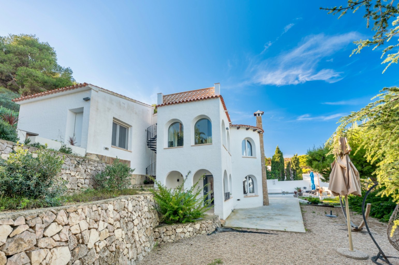 Witte gevel in mediterrane stijl met traditionele bogen, natuurstenen muren en een externe wenteltrap, gelegen in de zonnige omgeving van Jávea.