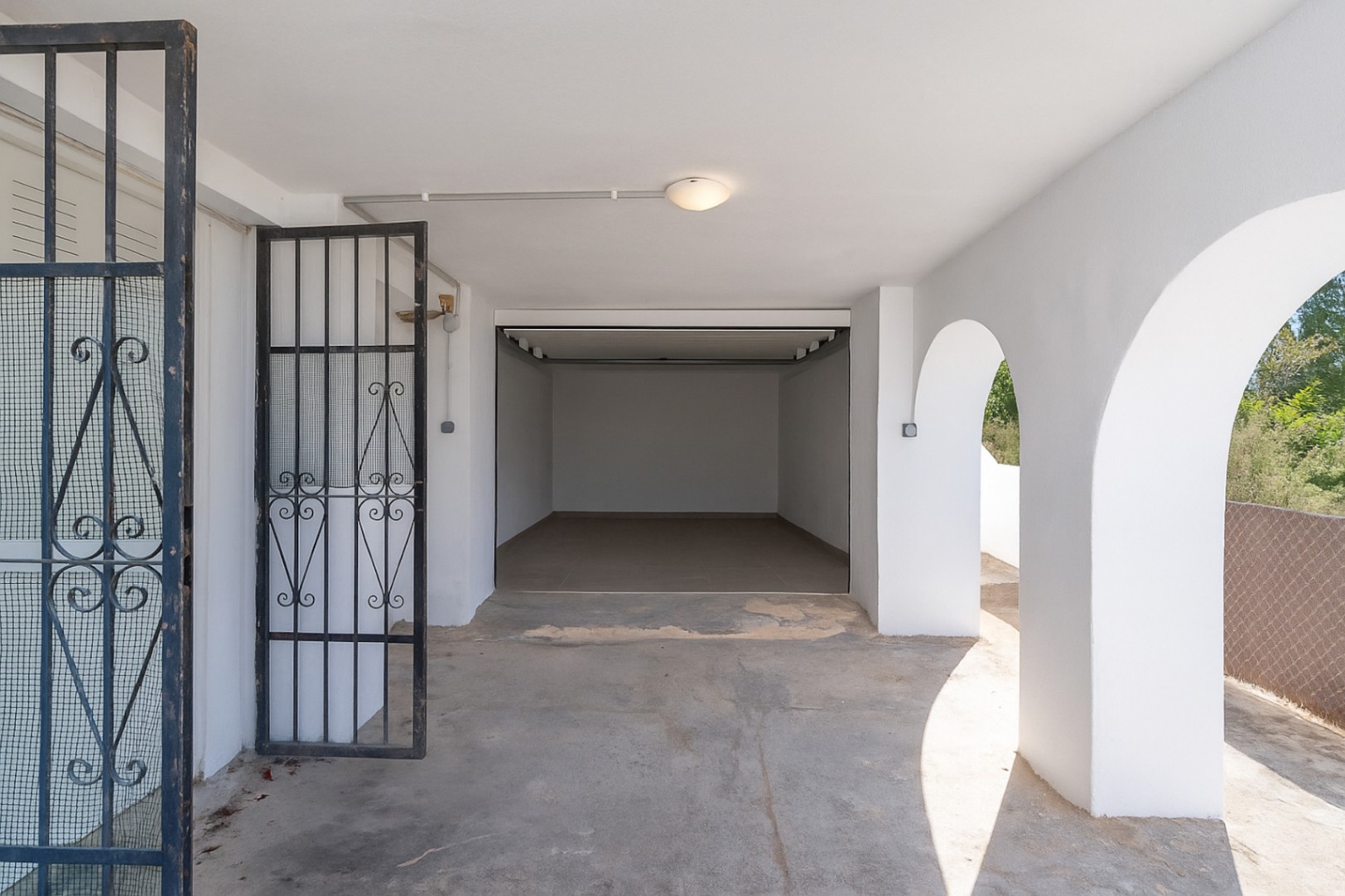 Afgesloten garage en overdekte parkeerplaats met mediterrane bogen, witte muren en een zwart smeedijzeren beveiligingshek.
