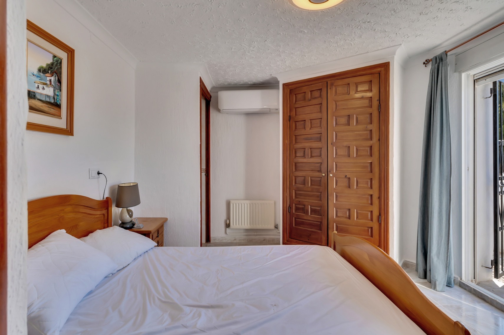 Lichte slaapkamer met een ingebouwde houten kledingkast, airconditioning en directe toegang tot het terras via een schuifpui.