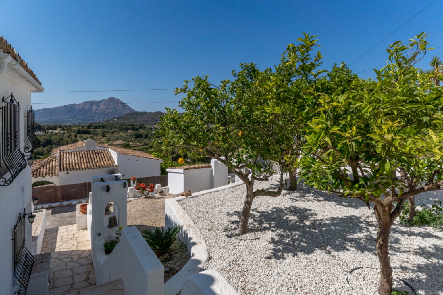 Mediterrane tuin met wit grind, citrusbomen en vrij uitzicht op de Montgó. Natuurstenen pad langs de traditionele witte architectuur van de woning.