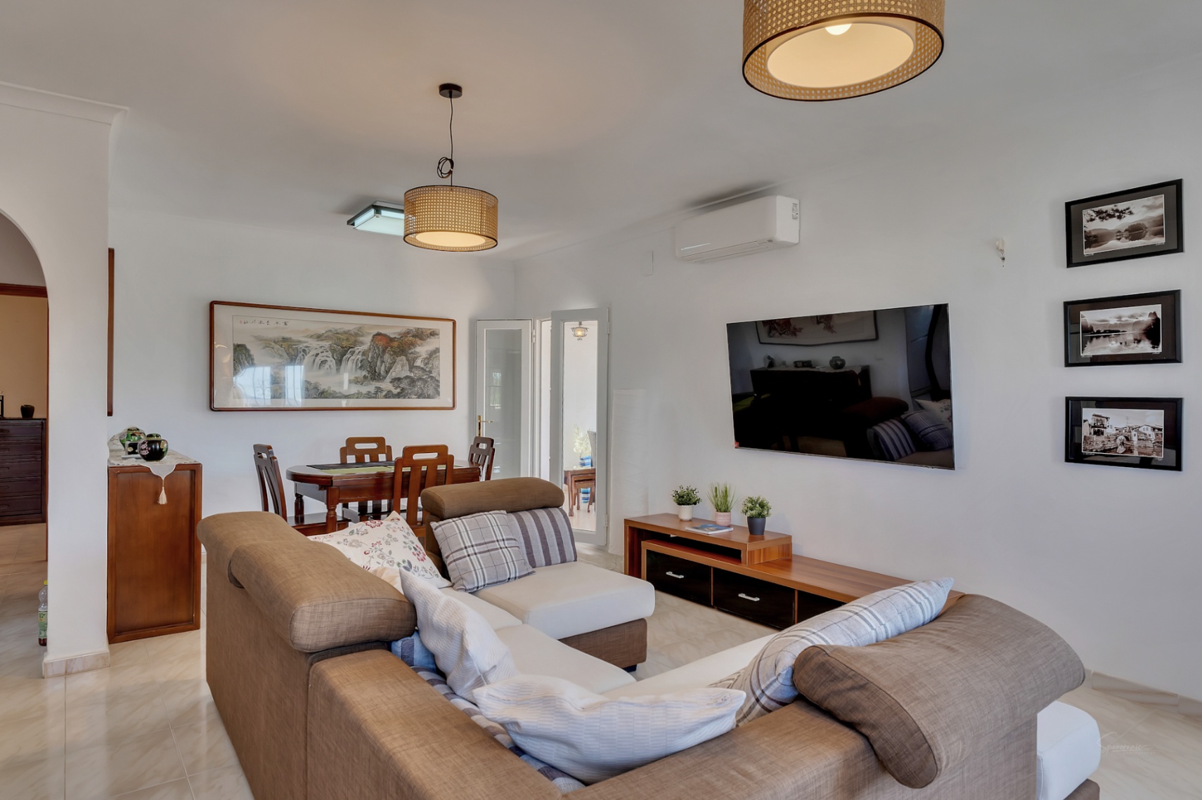 Open woon- en eetkamer met een ruime hoekbank, houten meubilair en hanglampen van natuurlijke vezels. Voorzien van airconditioning en een lichte tegelvloer.