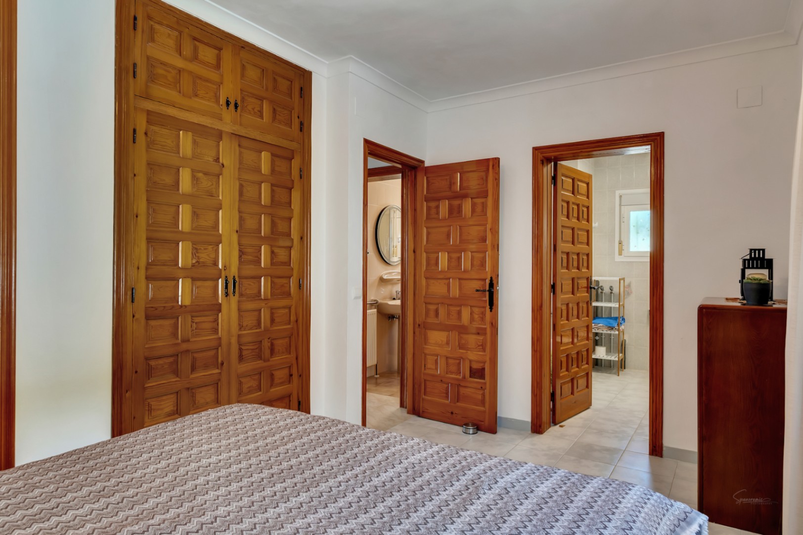 Slaapkamer met grote ingebouwde houten kasten met traditioneel houtsnijwerk en twee deuren die leiden naar de aangrenzende badkamers.
