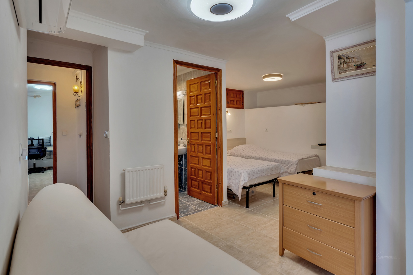 Slaapkamer met twee eenpersoonsbedden, een aangrenzende badkamer, wandradiator en een neutrale tegelvloer.