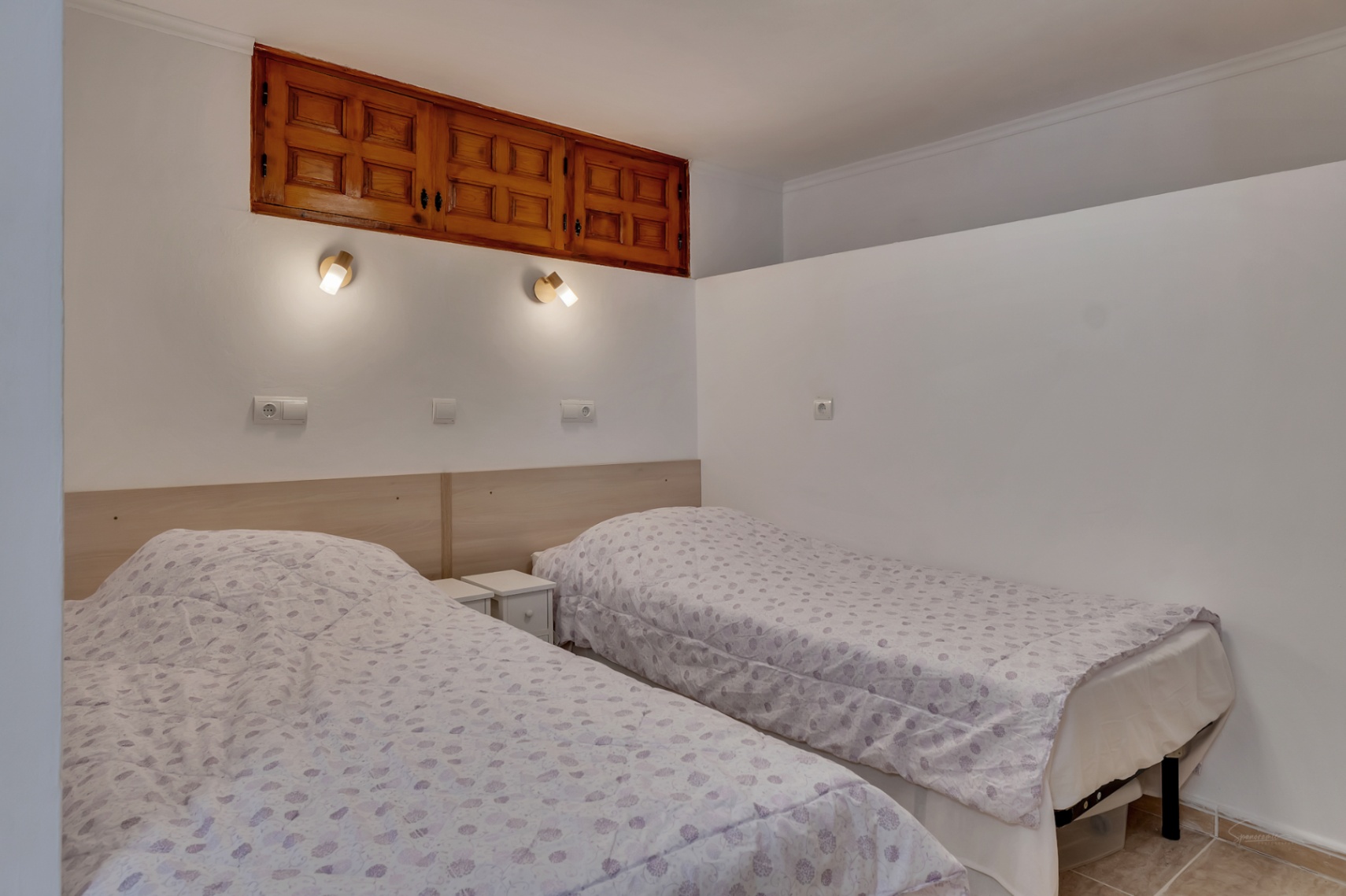 Slaapkamer met twee eenpersoonsbedden, licht houten hoofdbord en wandleeslampen. Een traditionele houten inbouwkast is in de bovenmuur geïntegreerd.