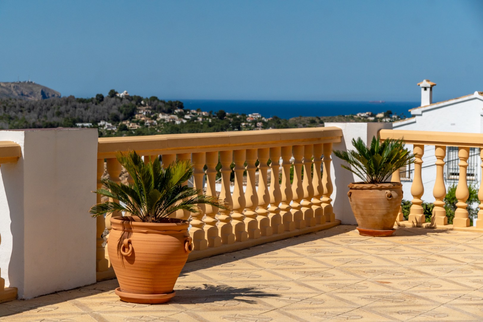 Verhoogd terras met gedecoreerde vloertegels, klassieke balustrade en terracotta potten met panoramisch uitzicht over de Middellandse Zee en de kustlijn.