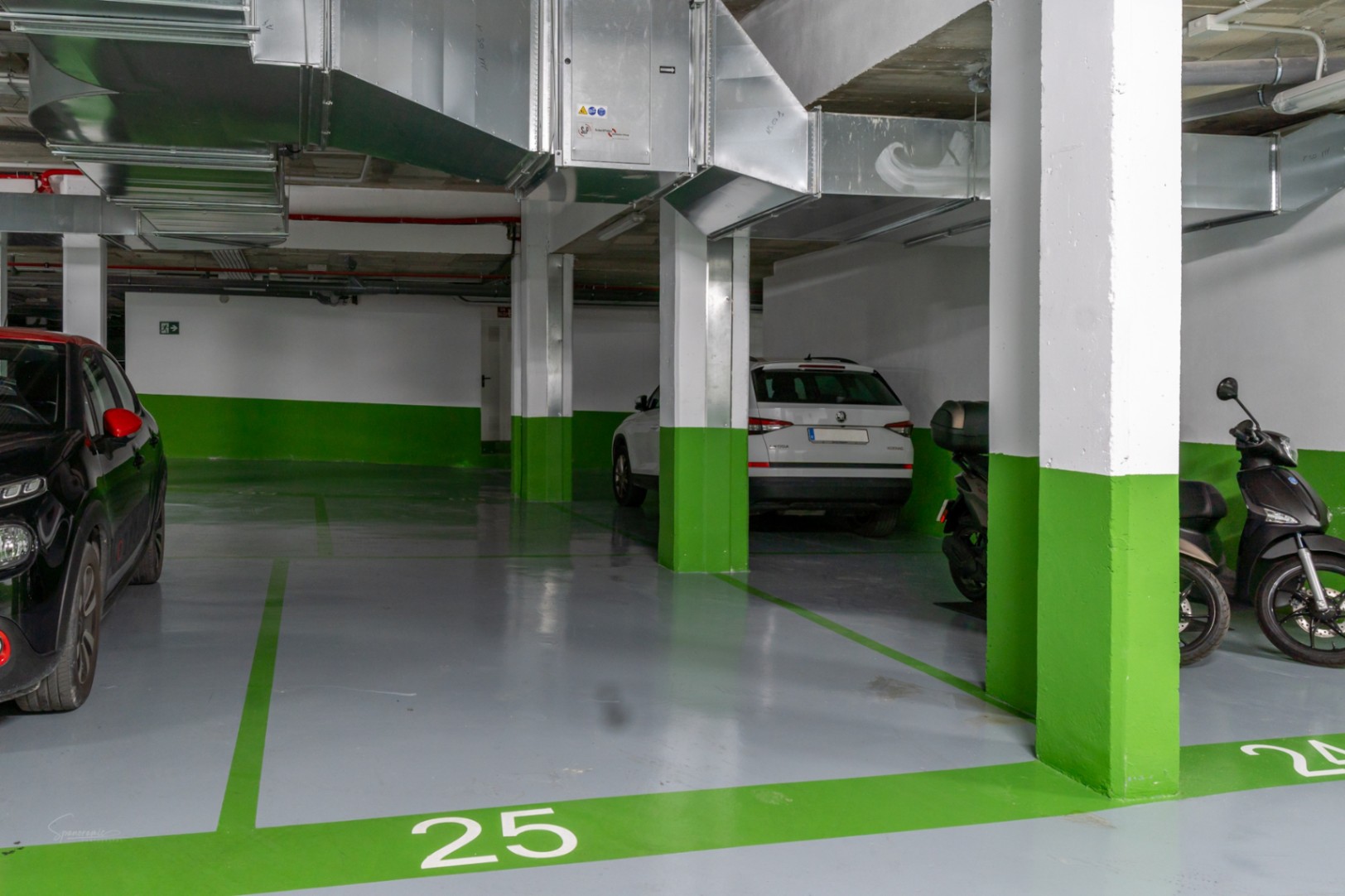 Genummerde ondergrondse parkeerplaats met een grijze gietvloer en groene accenten. Voorzien van betonnen kolommen en zichtbare ventilatiekanalen.