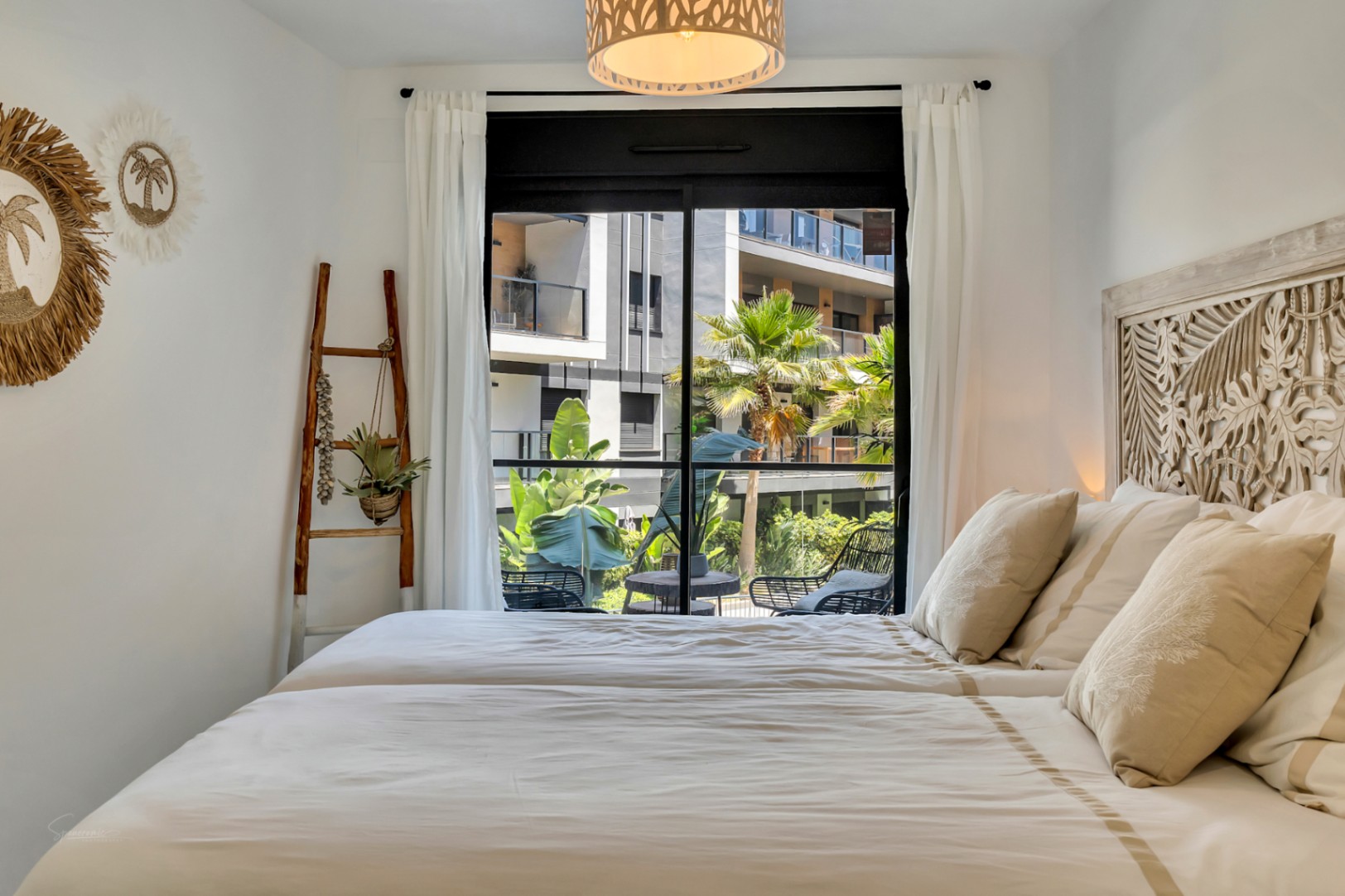 Lichte slaapkamer met een decoratief gesneden houten hoofdbord, mediterrane details en directe toegang tot een privéterras met uitzicht op de binnentuin.