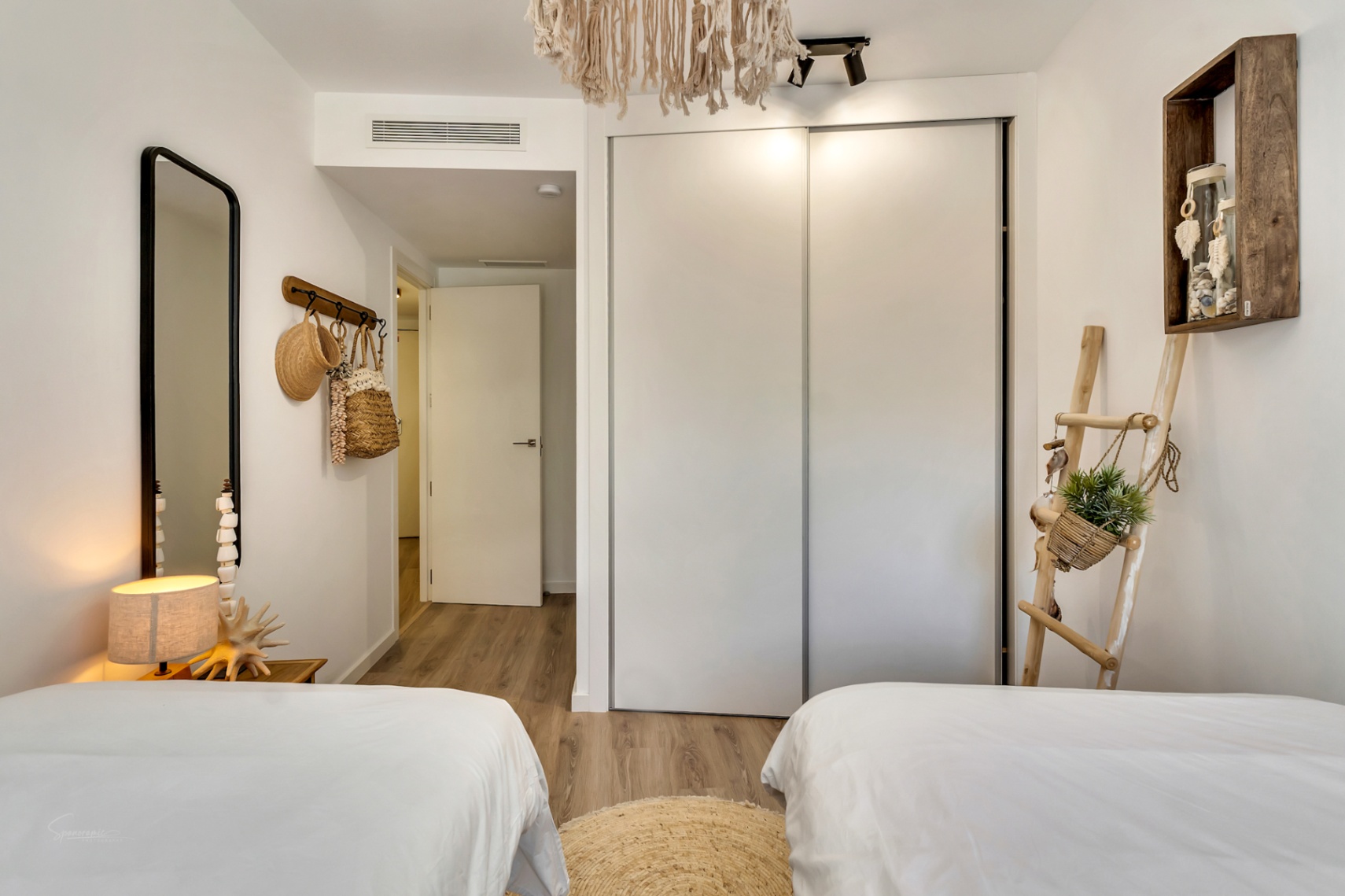 Lichte slaapkamer met twee eenpersoonsbedden, inbouwkast met schuifdeuren, lichte houten vloer en mediterrane decoratie met natuurlijke accenten.