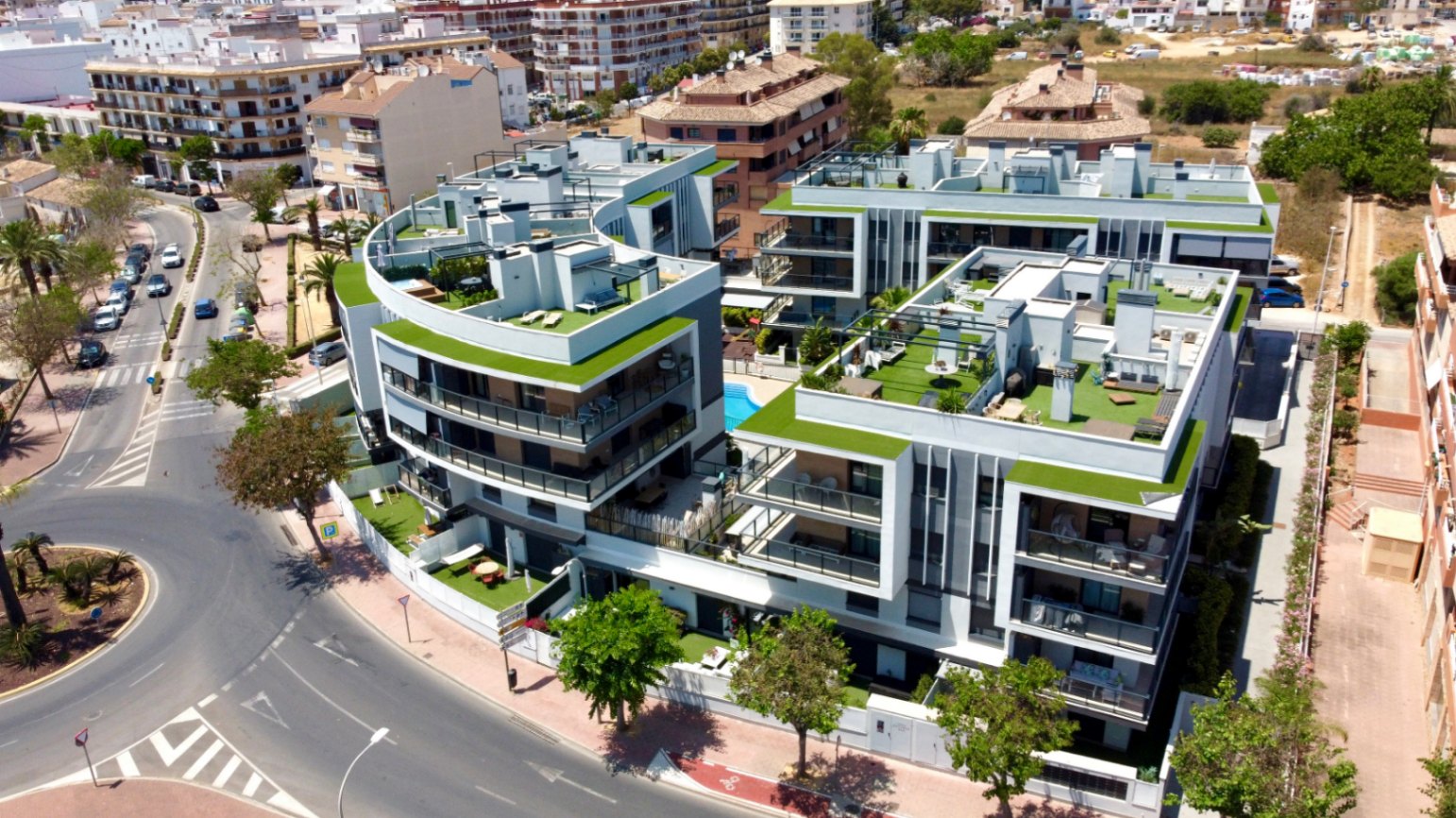 Luchtfoto van een modern wooncomplex in Jávea met gebogen gevels, ruime dakterrassen met kunstgras en een centraal gemeenschappelijk zwembad.