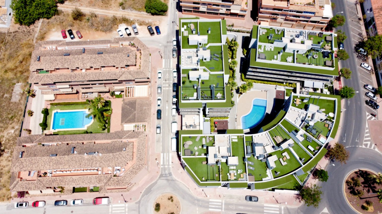 Luchtfoto van het moderne wooncomplex in Jávea, met de gebogen architectuur, ruime dakterrassen met kunstgras en een centraal gemeenschappelijk zwembad.