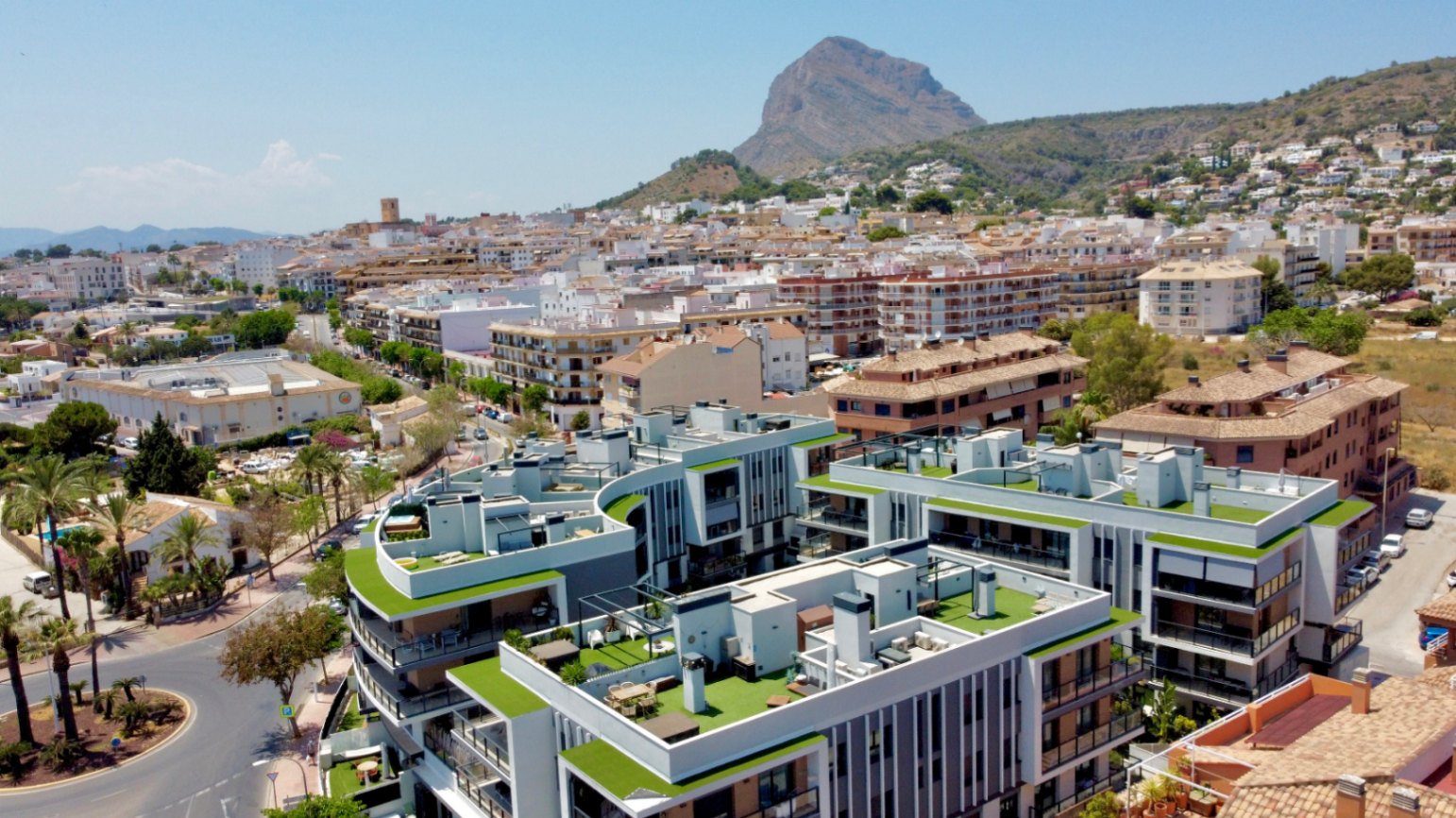 Luchtfoto van het moderne wooncomplex in Jávea, met groene dakterrassen en een panoramisch uitzicht op de berg Montgó en het oude stadscentrum.