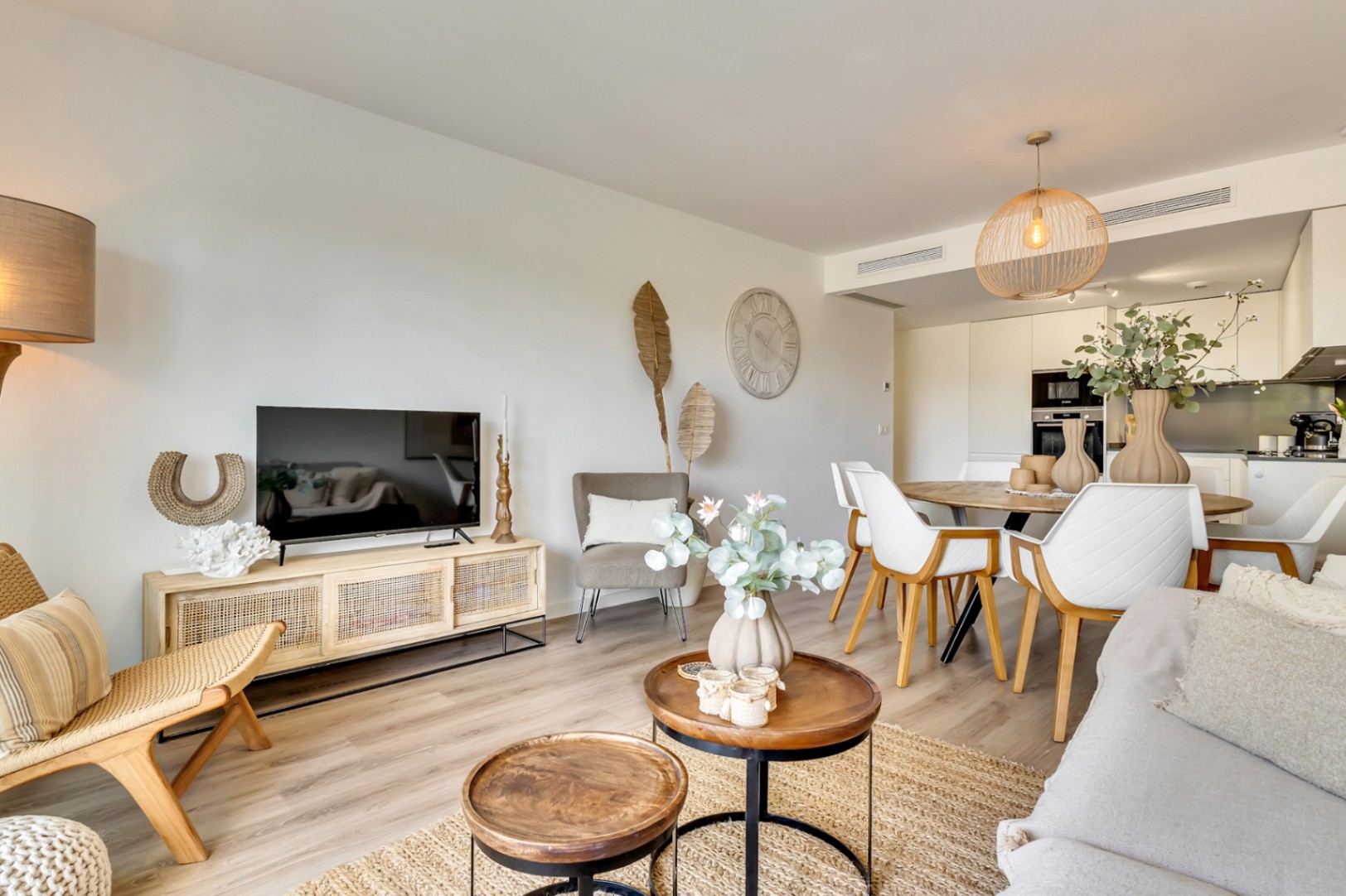 Open woon- en eetkamer met houten vloeren, natuurlijke accenten en een moderne geïntegreerde keuken met witte kasten.