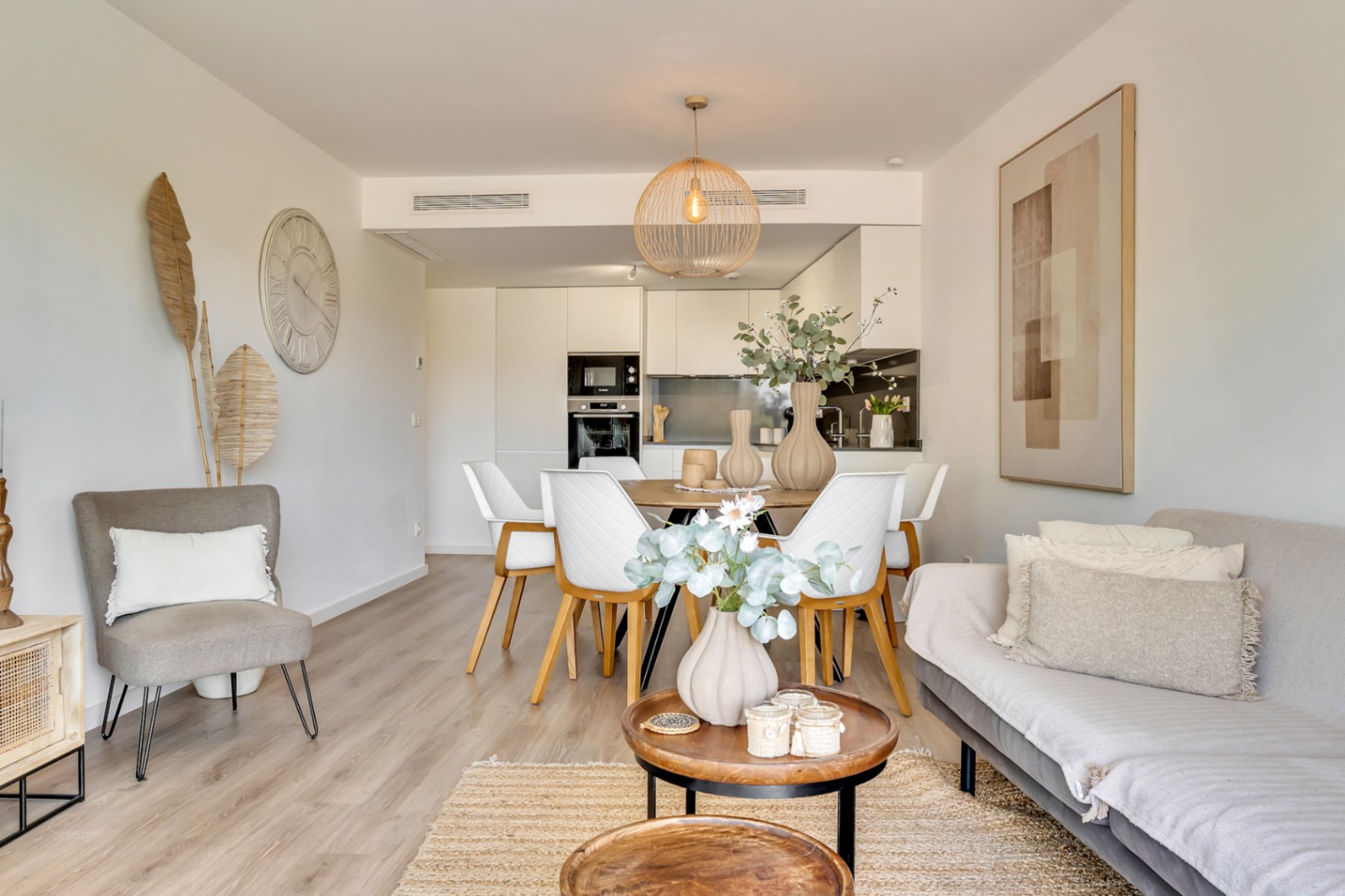 Open woonruimte met een lichte houten vloer, een moderne keuken en een eethoek. Het interieur is ingericht met neutrale tinten, natuurlijke materialen en eigentijdse verlichting.