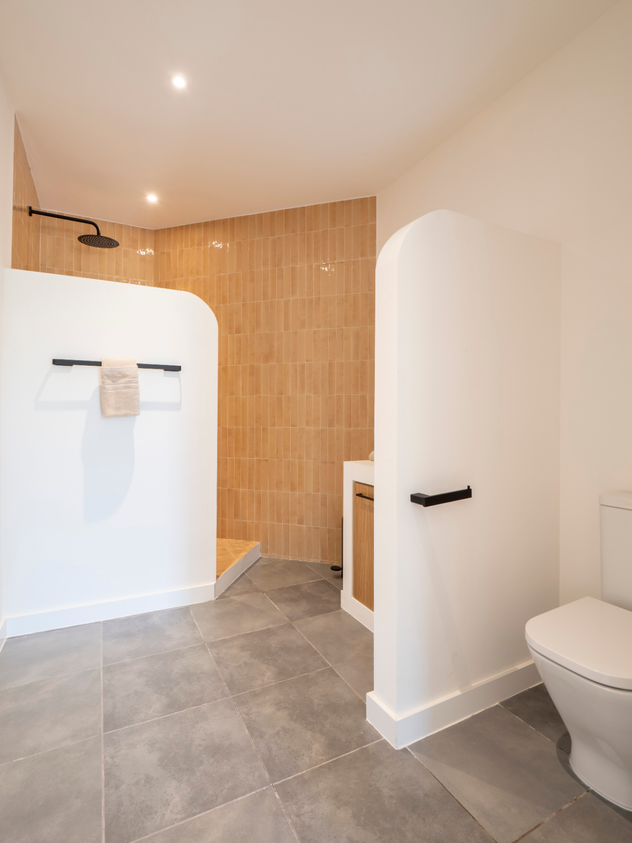 Badkamer met inloopdouche en okerkleurige tegels. Houten wastafelmeubel en grijze tegelvloer.
