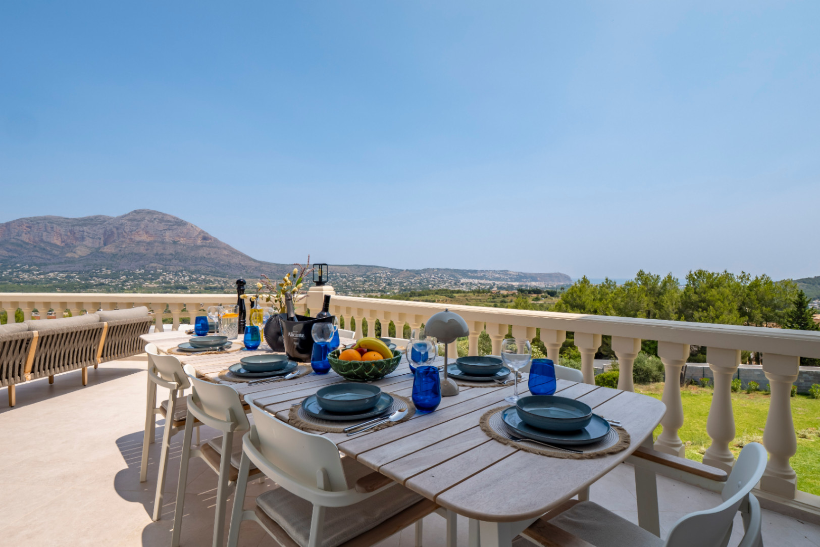 Eethoek buiten met houten tafel en panoramisch uitzicht op de bergen en de kust vanaf het terras.