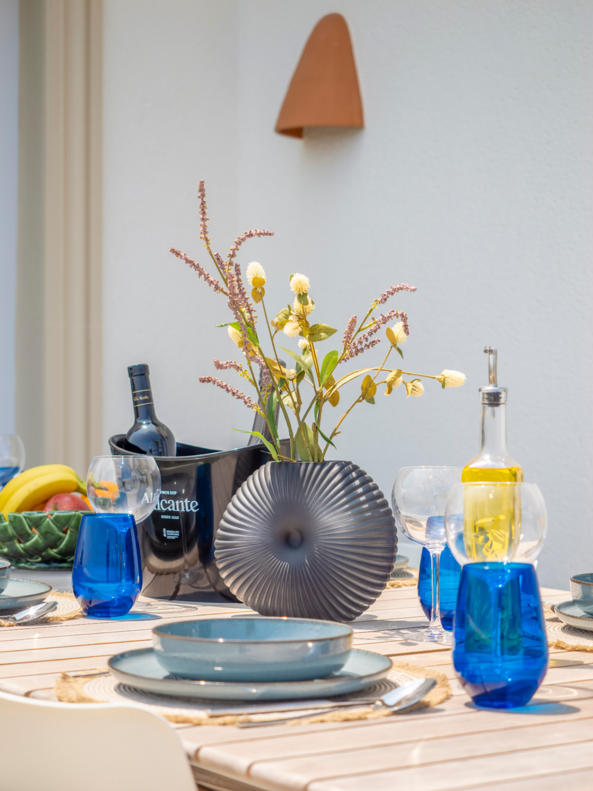Eettafel buiten met blauw servies, een grijze vaas en een Alicante wijnkoeler.