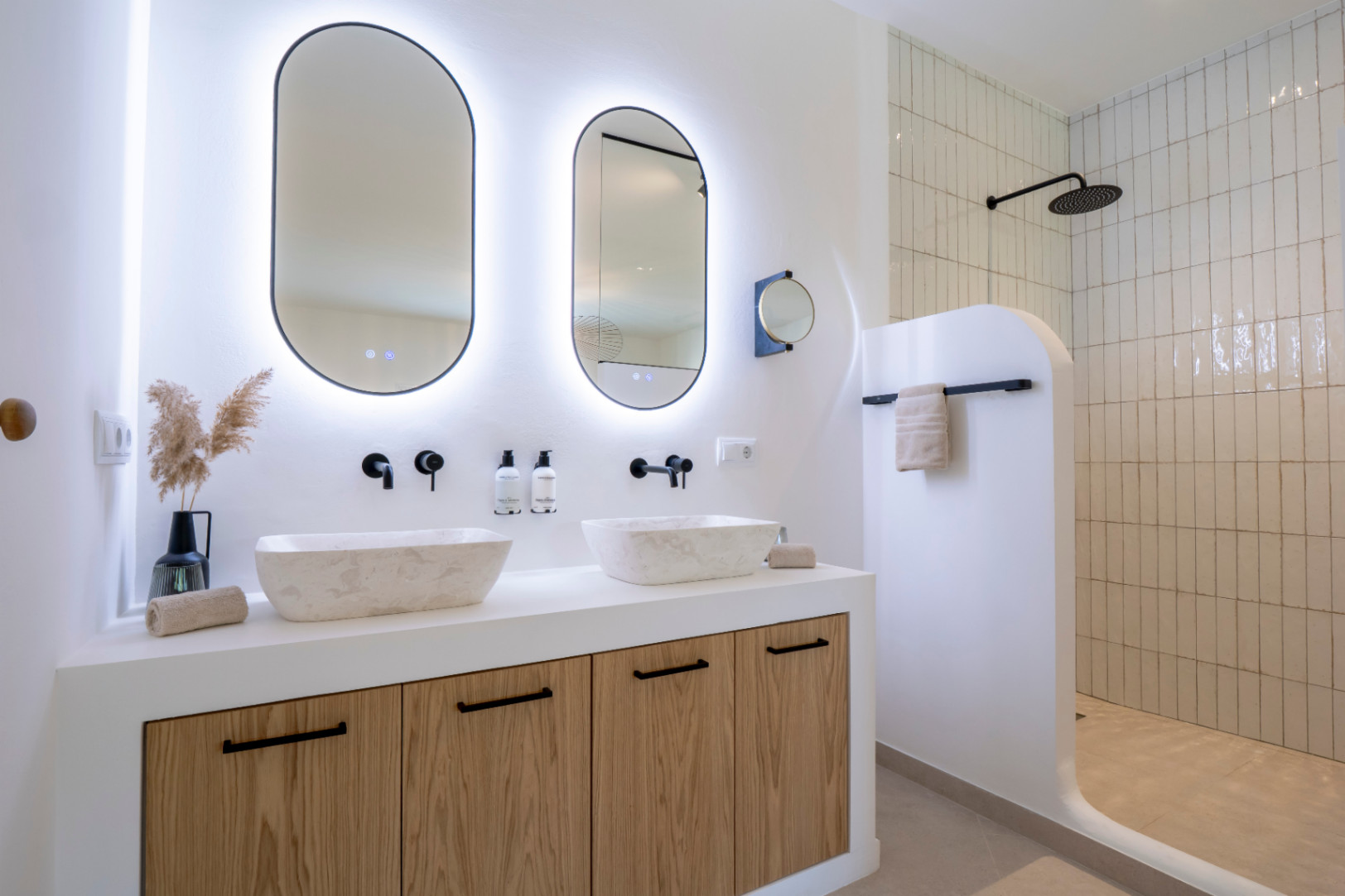 Elegante badkamer met stenen wastafels, ovale spiegels met verlichting en een douche met verticale tegels.
