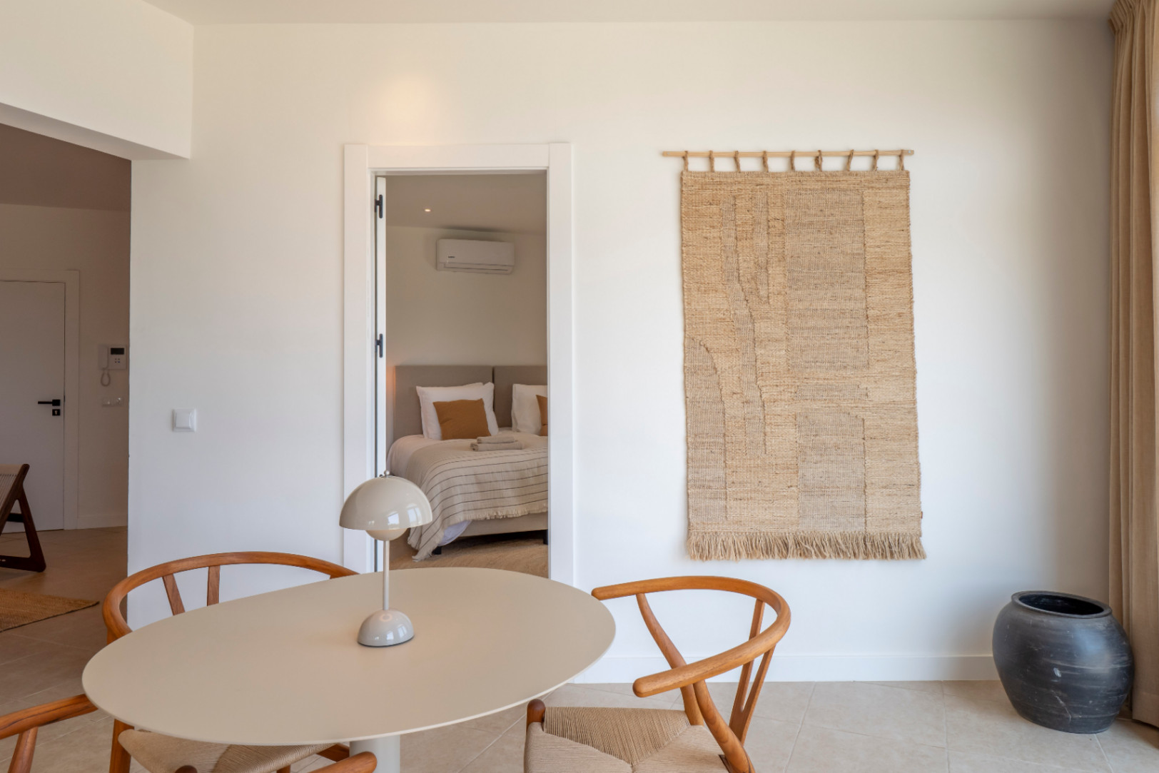 Interieurdetail met ronde tafel, houten stoelen en doorkijk naar de slaapkamer.