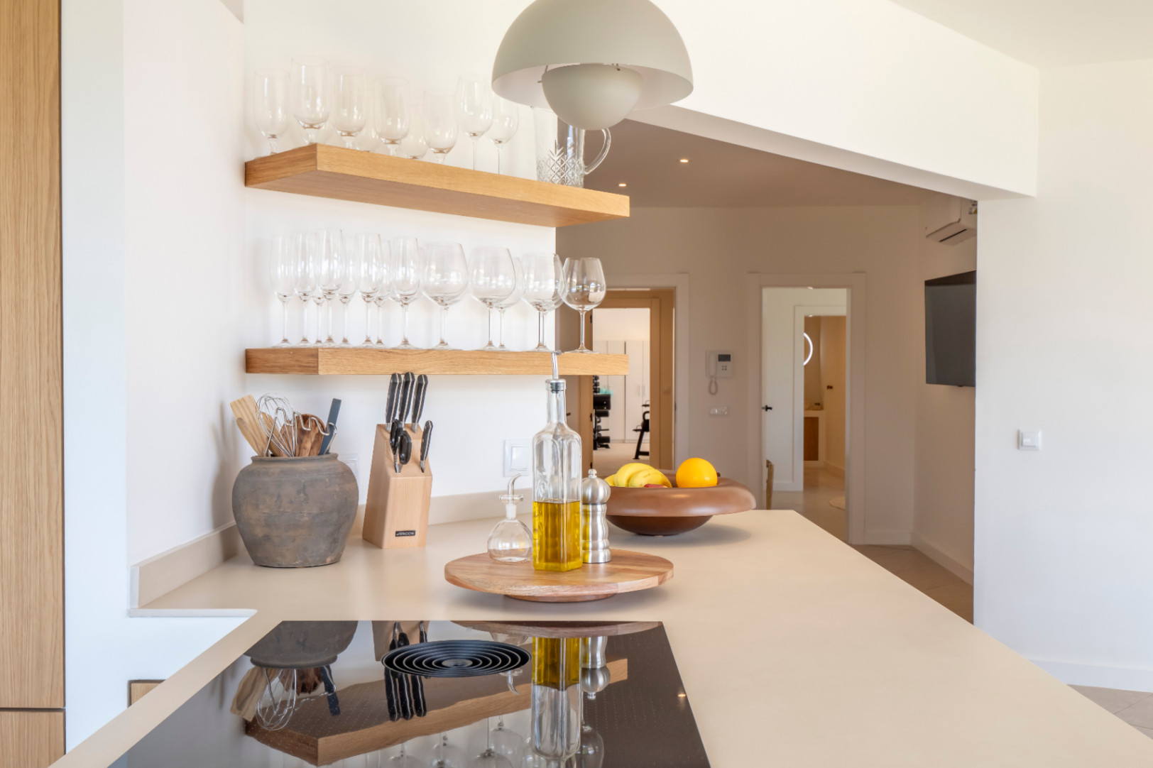 Keukendetail: lichte houten planken met glazen, beige aanrechtblad met inductiekookplaat en minimalistische inrichting.