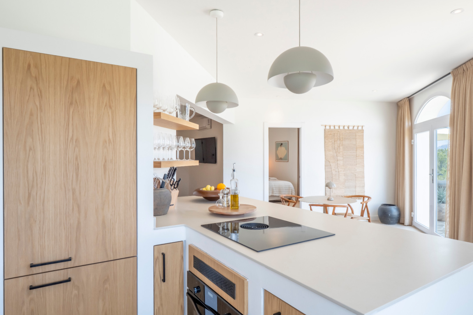 Keukendetail met eiland, licht houten panelen op apparaten en open planken met glaswerk.