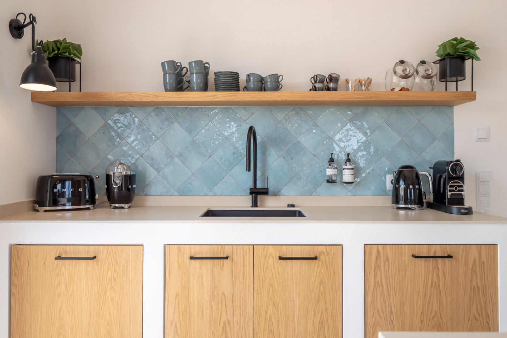 Keukendetail met wastafel, turquoise tegels en Smeg-apparatuur. Lichte houten planken.