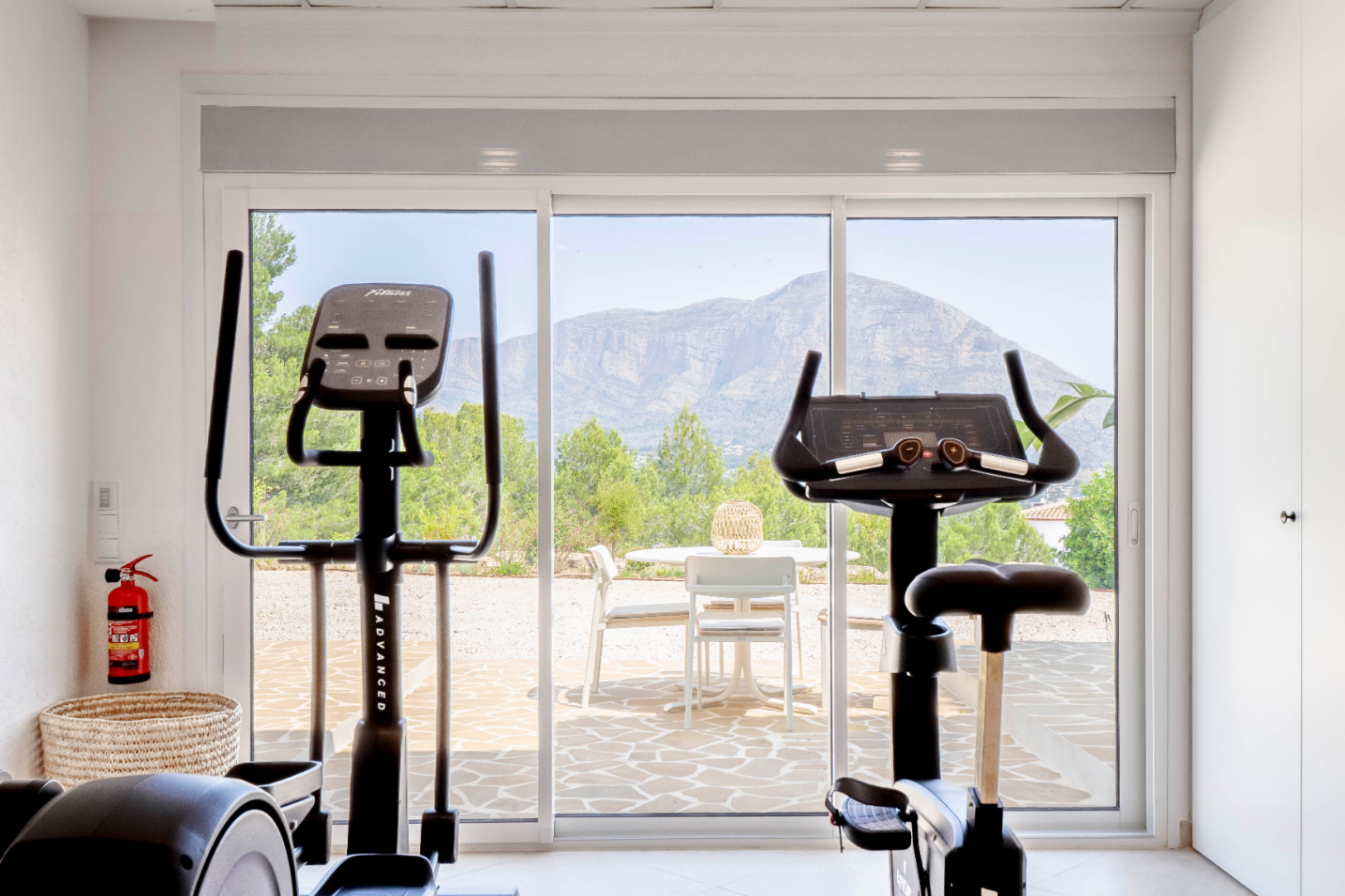 Lichte fitnessruimte met uitzicht op de bergen, uitgerust met hometrainer en elliptische trainer.