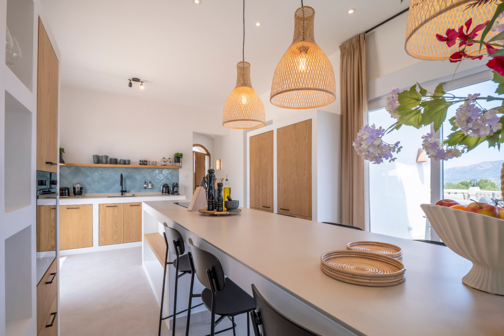 Lichte keuken met centraal eiland, rieten lampen en lichte houten meubels. Turquoise tegels op de muur.