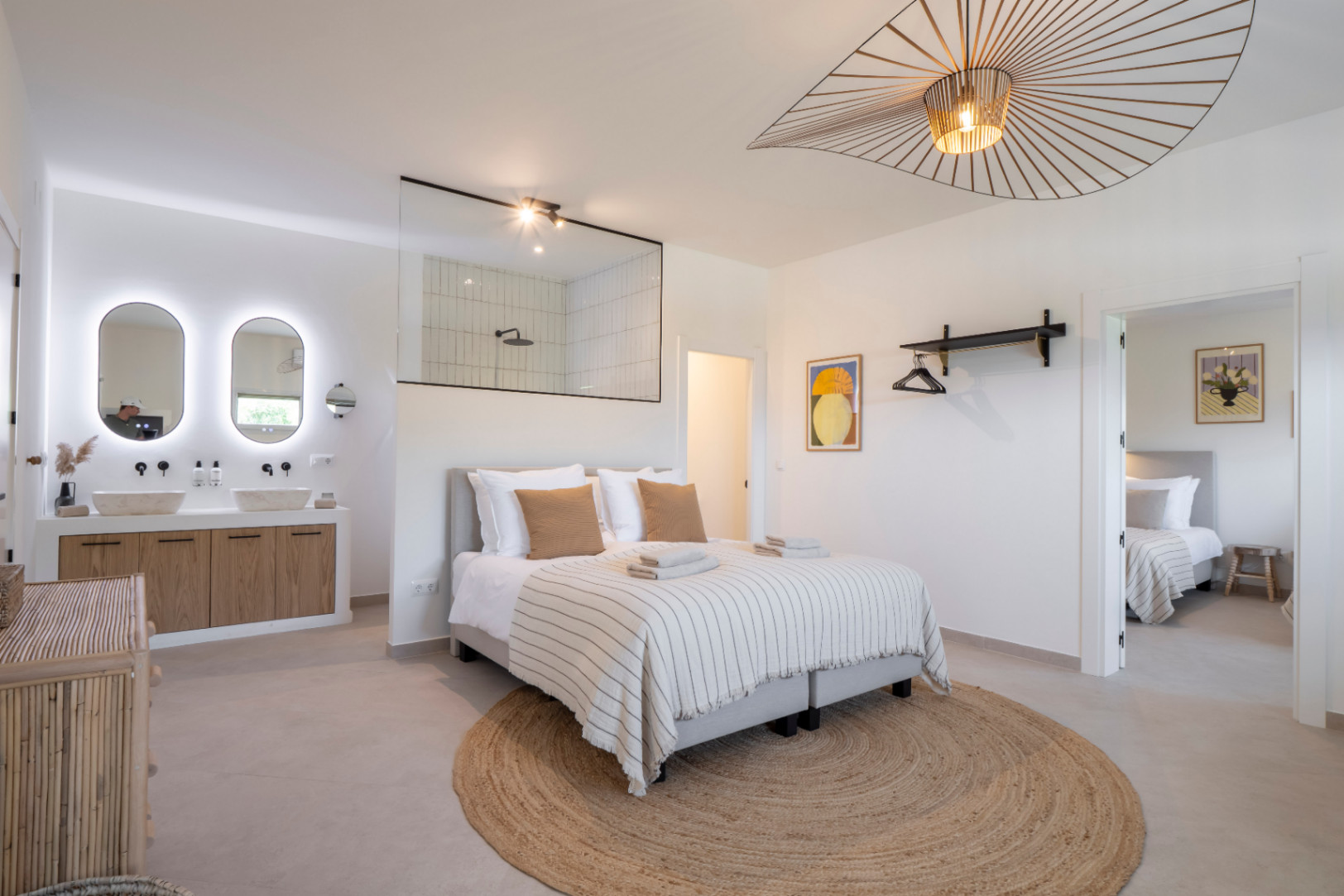 Lichte slaapkamer met geïntegreerde badkamer en dubbele wastafel met verlichte spiegels.