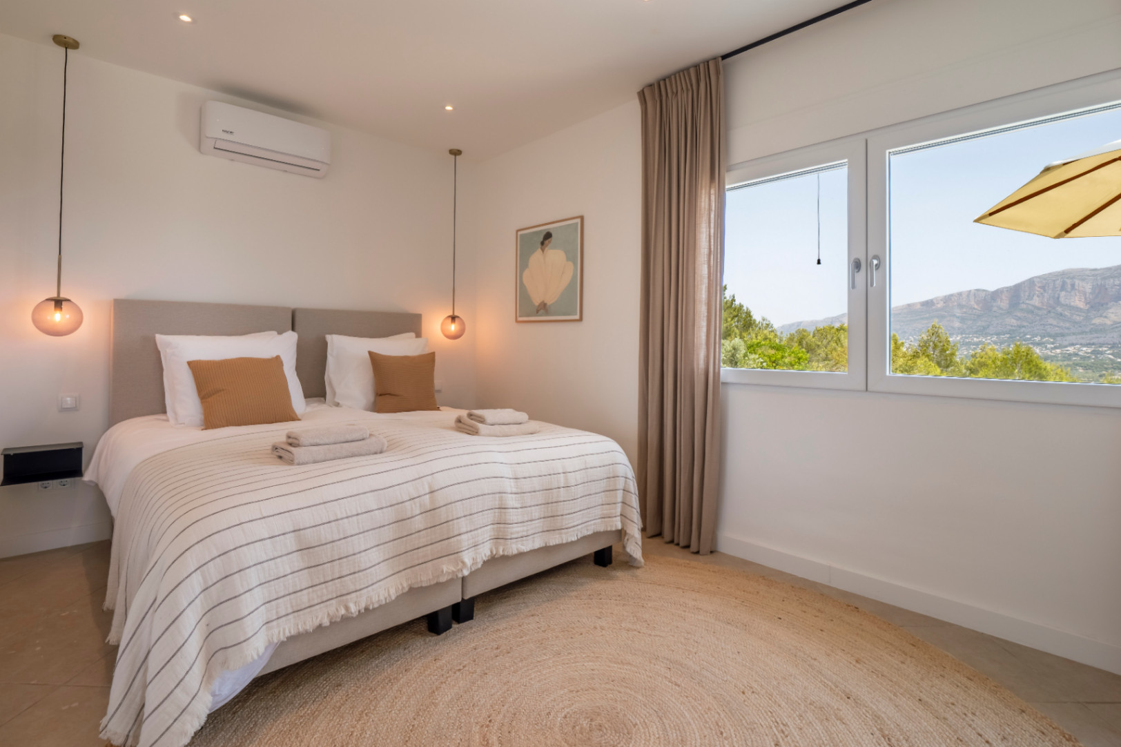 Lichte slaapkamer met rond jute vloerkleed en uitzicht op de bergen.