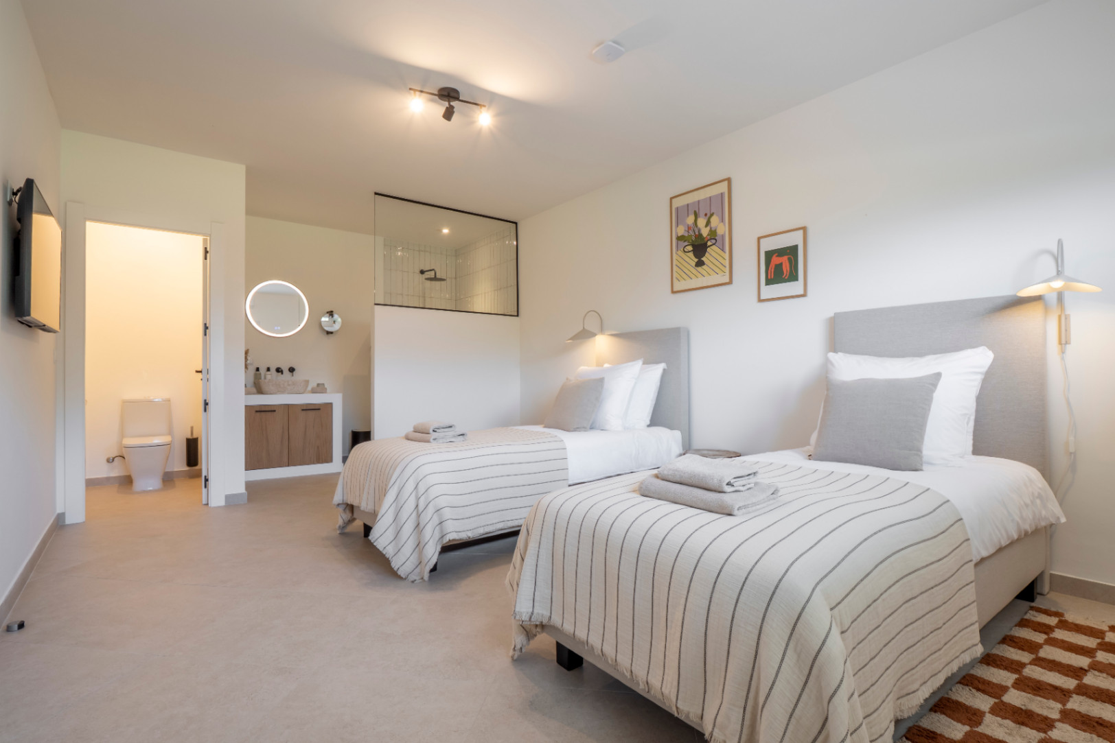 Lichte slaapkamer met twee eenpersoonsbedden, en-suite badkamer met glazen douche en licht houten wastafel.