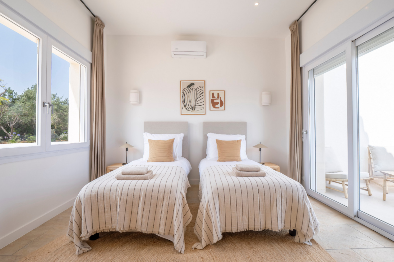 Lichte slaapkamer met twee eenpersoonsbedden, gestreepte lakens en minimalistische inrichting. Toegang tot een buitenterras.