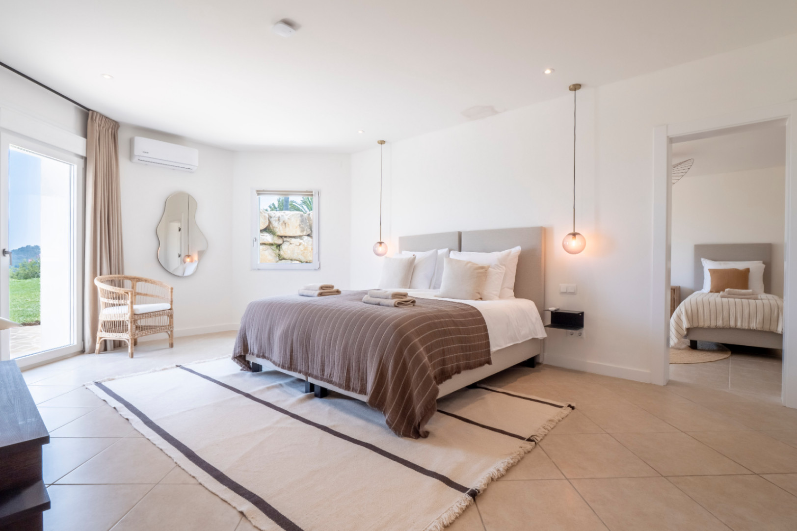 Lichte slaapkamer met tweepersoonsbed, gestreept vloerkleed en uitzicht op de tuin.