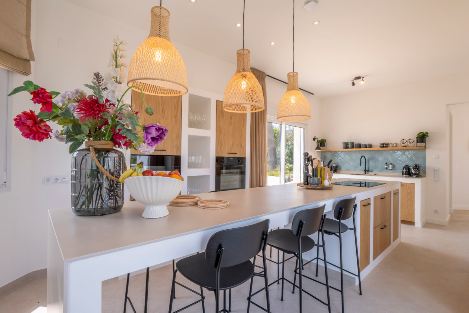 Moderne keuken met centraal eiland, zwarte krukken en hanglampen van wicker.