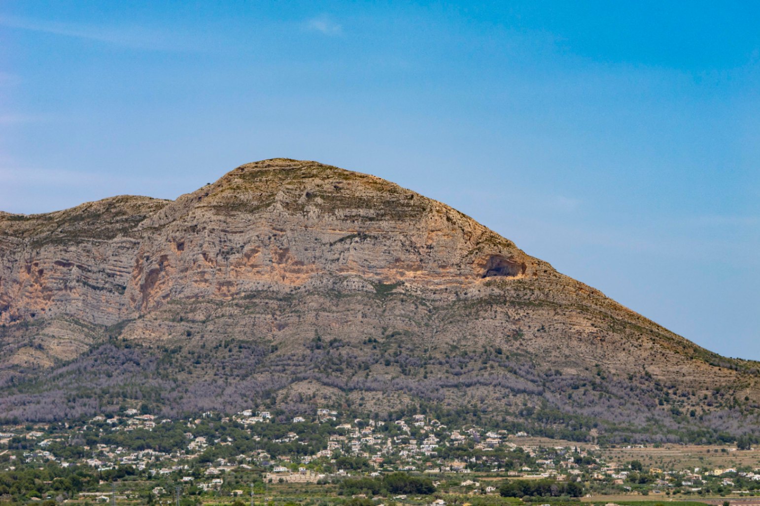 Panoramisch uitzicht op de Montgó berg, met een zichtbare grot en verspreide huizen aan de voet.