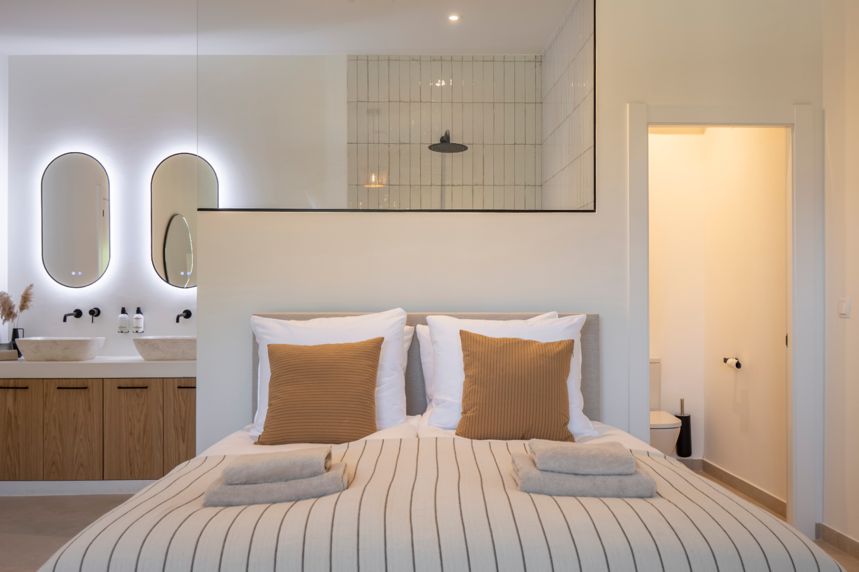 Slaapkamer met en-suite badkamer. Stenen wastafels op licht houten kast en LED-verlichting.