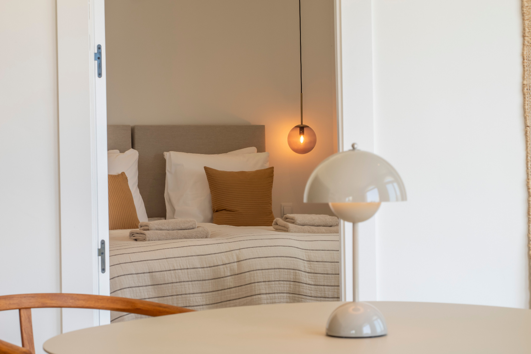 Slaapkamer met tweepersoonsbed, bolvormige hanglamp en gestreept beddengoed. Ronde tafel met paddenstoel tafellamp.
