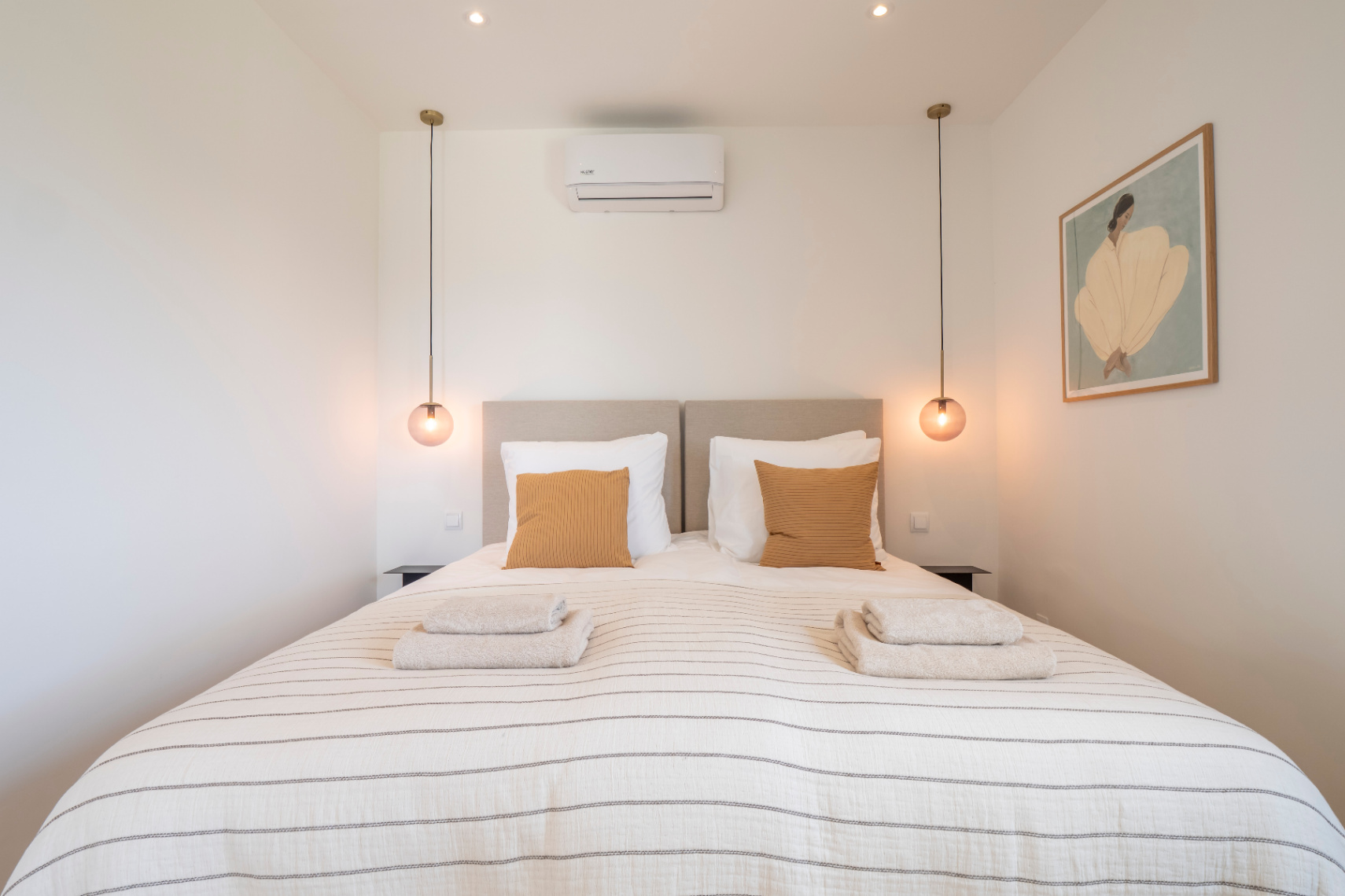 Slaapkamer met tweepersoonsbed, gestreept beddengoed en bolvormige hanglampen.