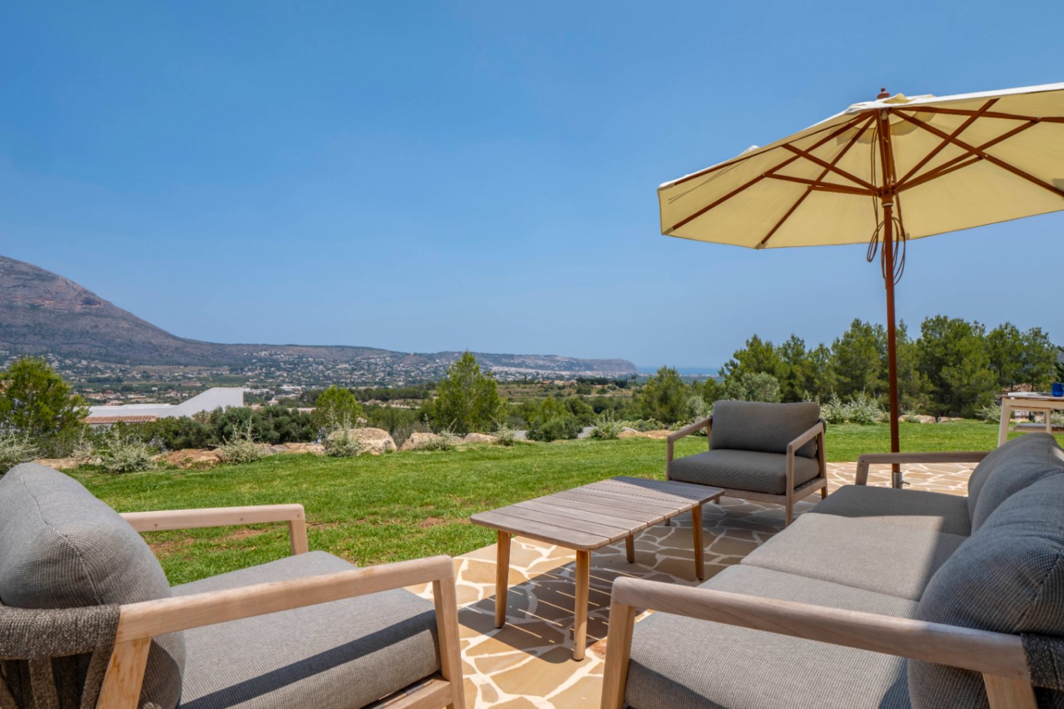 Terras met uitzicht: stenen en houten tuinmeubilair onder een parasol, met uitzicht op Jávea.