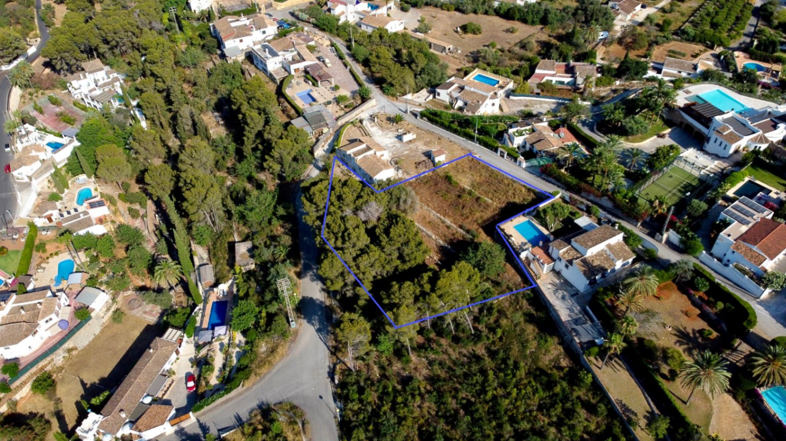 Luchtfoto van het blauw omkaderde bouwperceel van 1.908 m², met een combinatie van pijnbomen en open ruimte in een gevestigde woonwijk in Jávea.