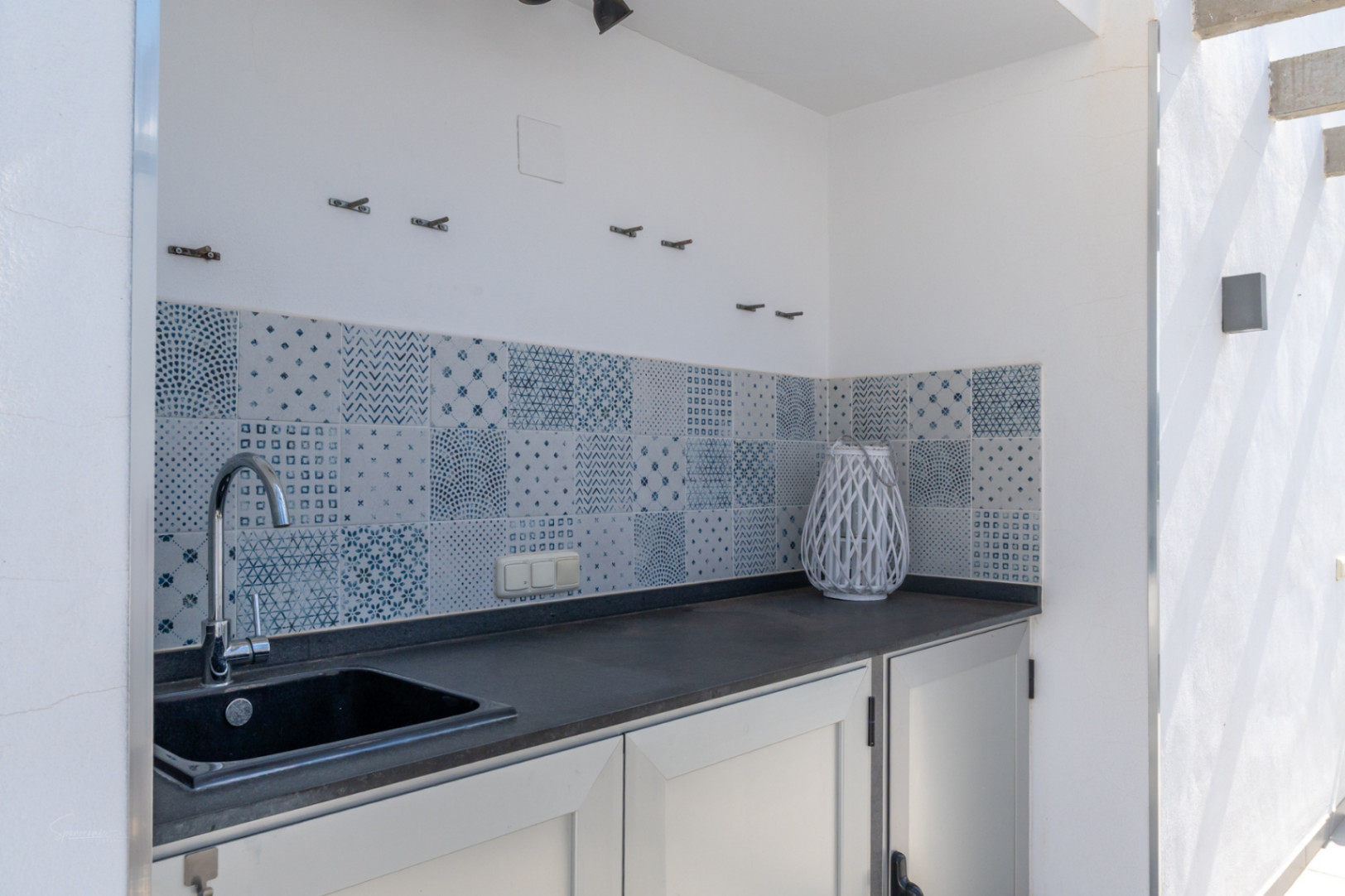 Buitenkeuken op het terras met een donker werkblad, geïntegreerde spoelbak en een decoratieve achterwand van blauw-witte tegels.
