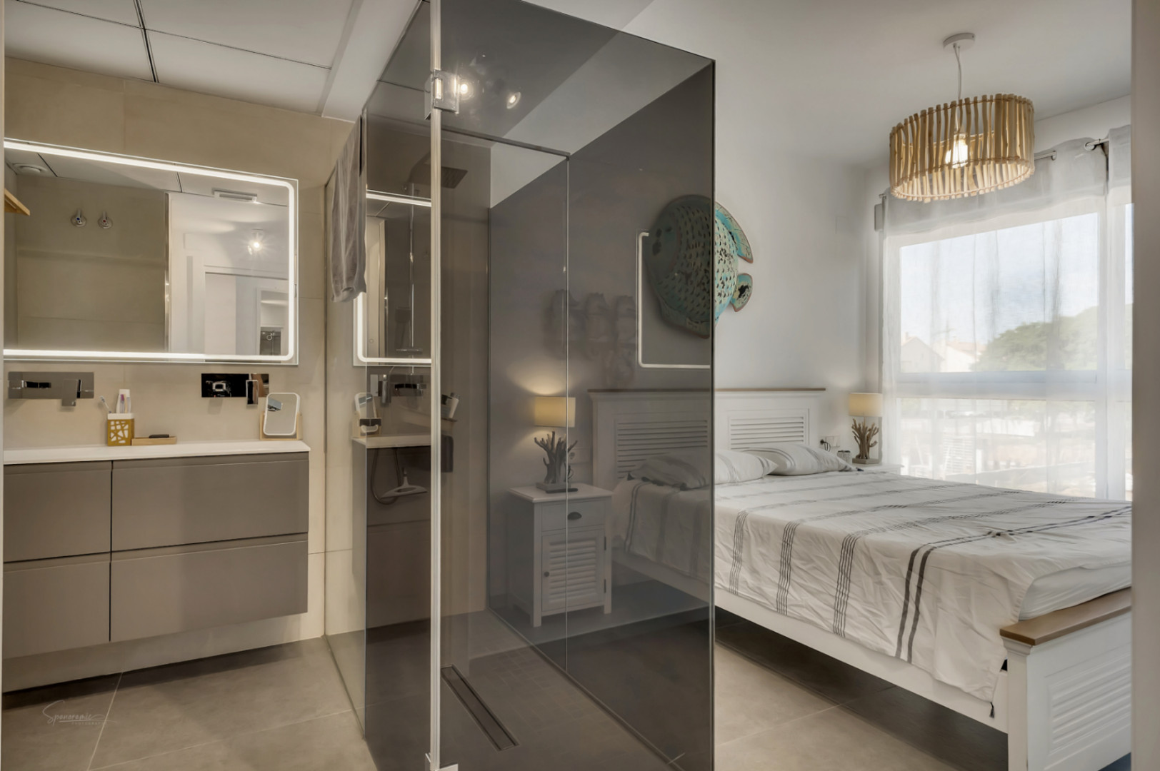 Hoofdslaapkamer met geïntegreerde badkamer, gescheiden door een rookglazen wand, voorzien van een zwevend badmeubel, verlichte spiegel en houten hanglamp.