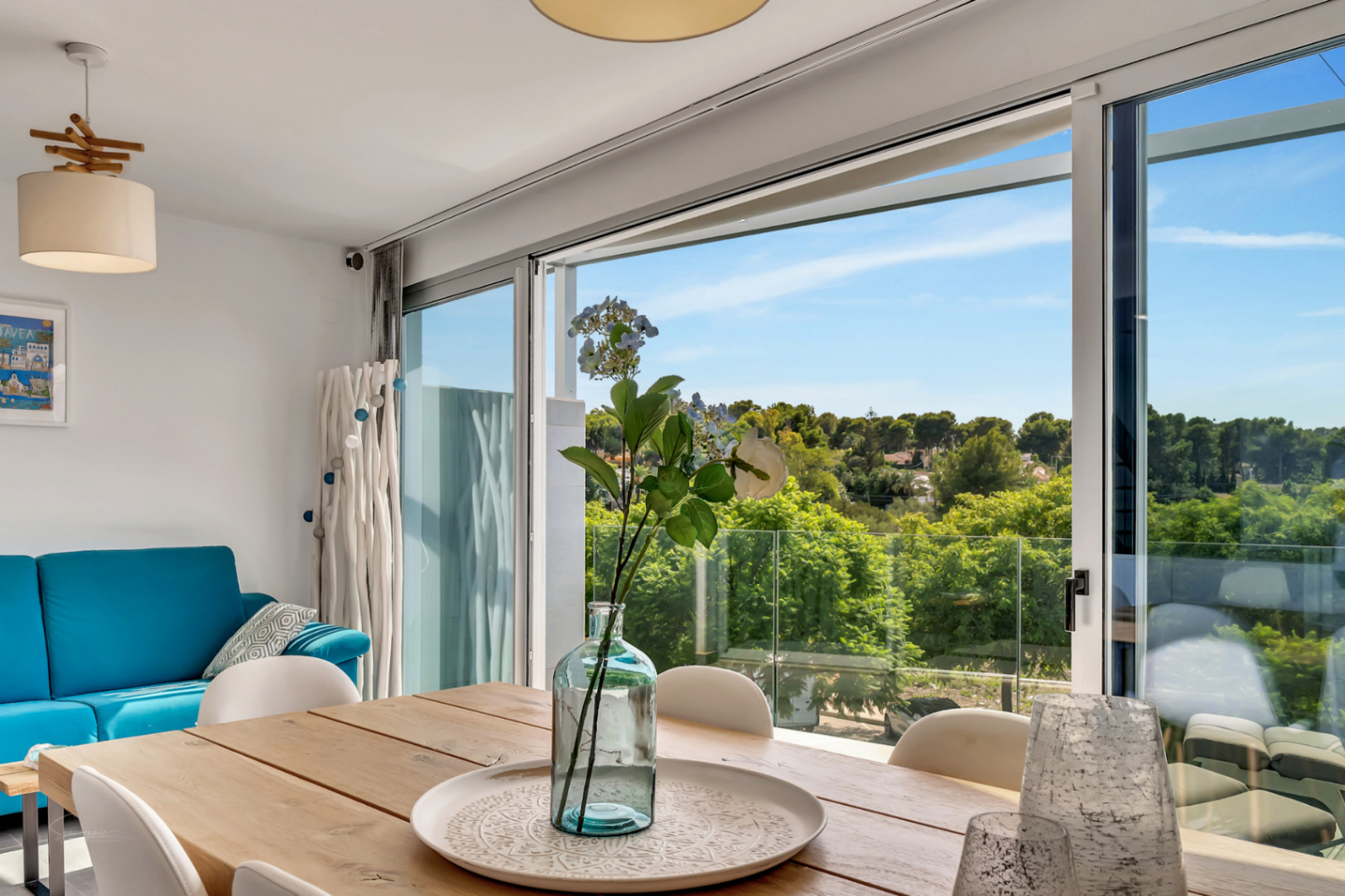 Lichte eetkamer met houten tafel en grote glazen schuifdeuren die een weids uitzicht bieden op de groene omgeving en toegang geven tot het balkon.