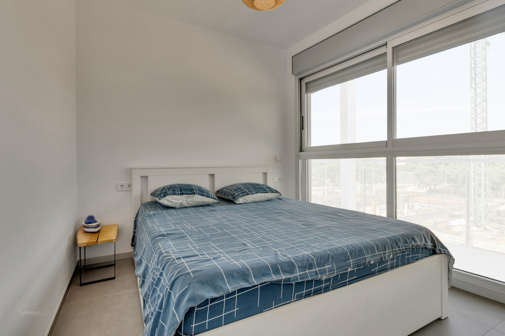 Lichte slaapkamer met tweepersoonsbed, grote schuiframen met grijze kozijnen en elektrische rolluiken in een modern, strak interieur.
