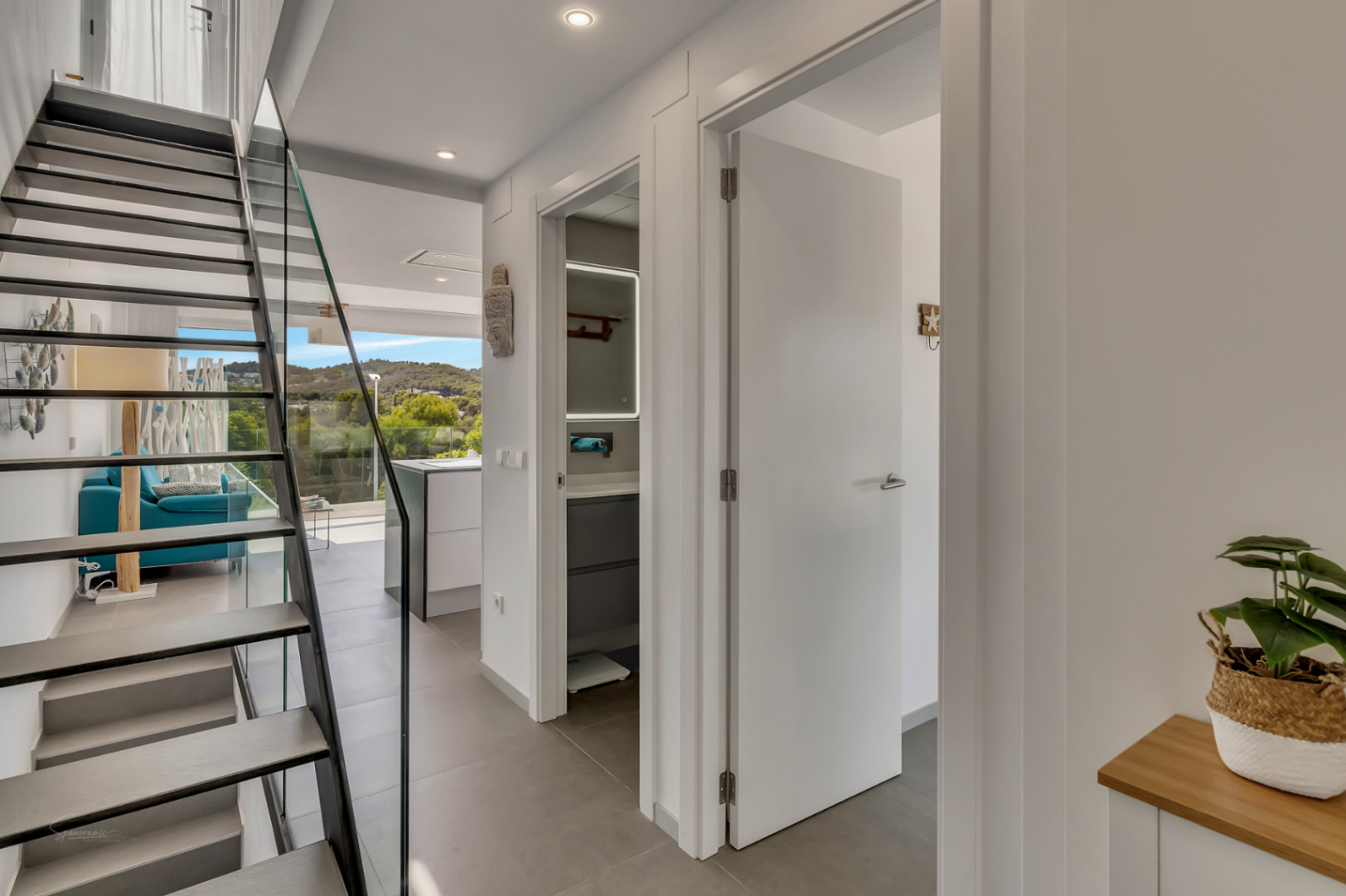 Moderne hal met een open trap met glazen balustrade, die toegang biedt tot de lichte woonkamer met uitzicht op het omliggende landschap.