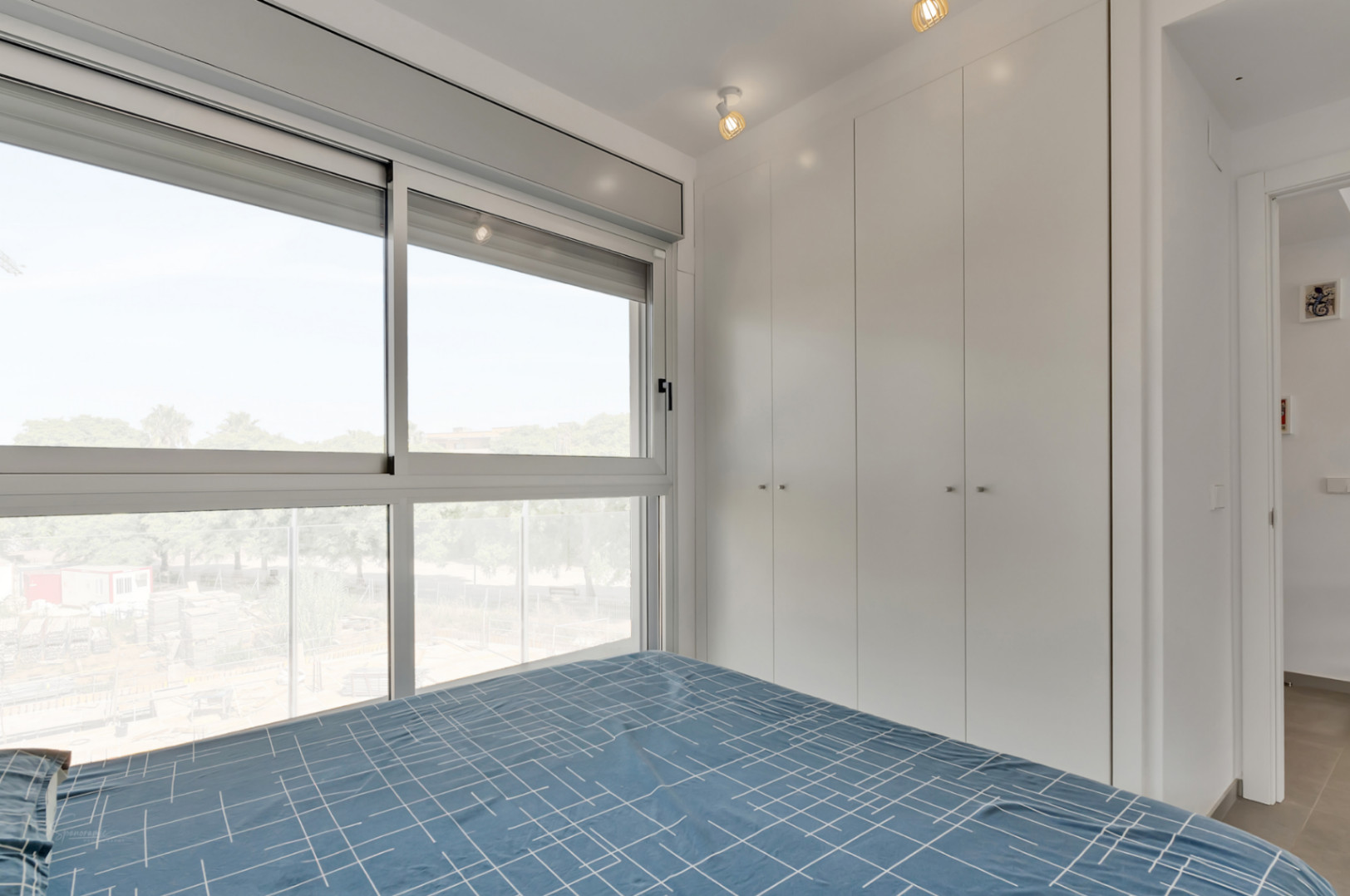 Moderne slaapkamer met kamerhoge witte inbouwkasten en een groot raam met gemotoriseerde rolluiken voor veel natuurlijk licht.