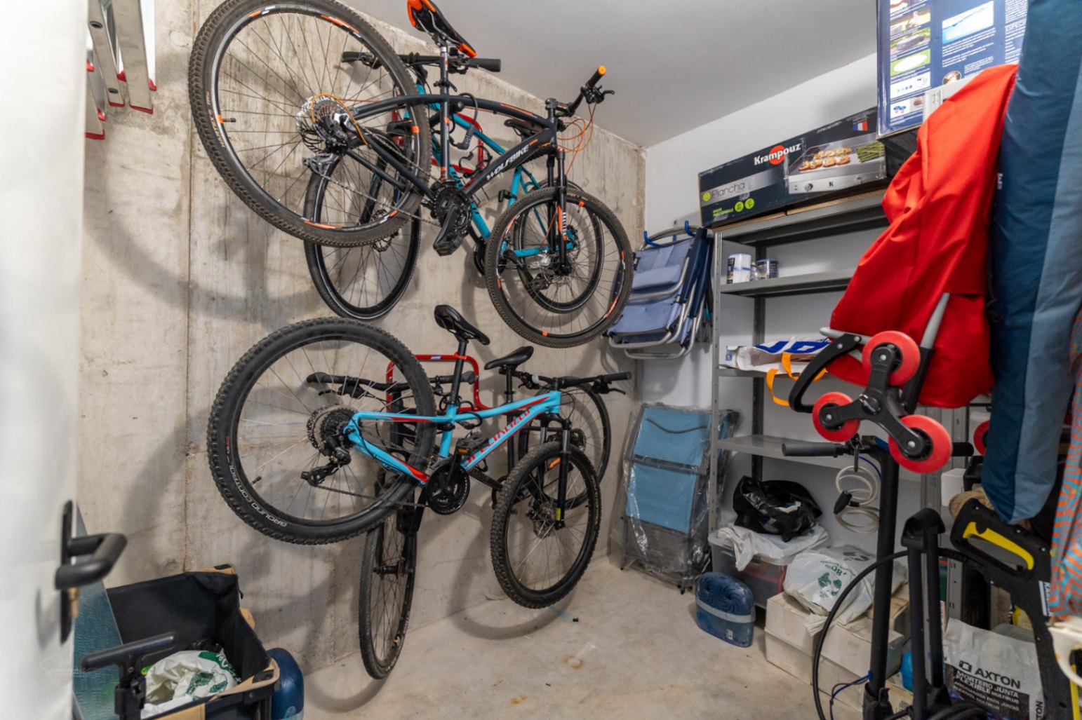 Privé berging met wanden van zichtbeton, voorzien van wandhouders voor fietsen en metalen stellingen voor een georganiseerde opslag.